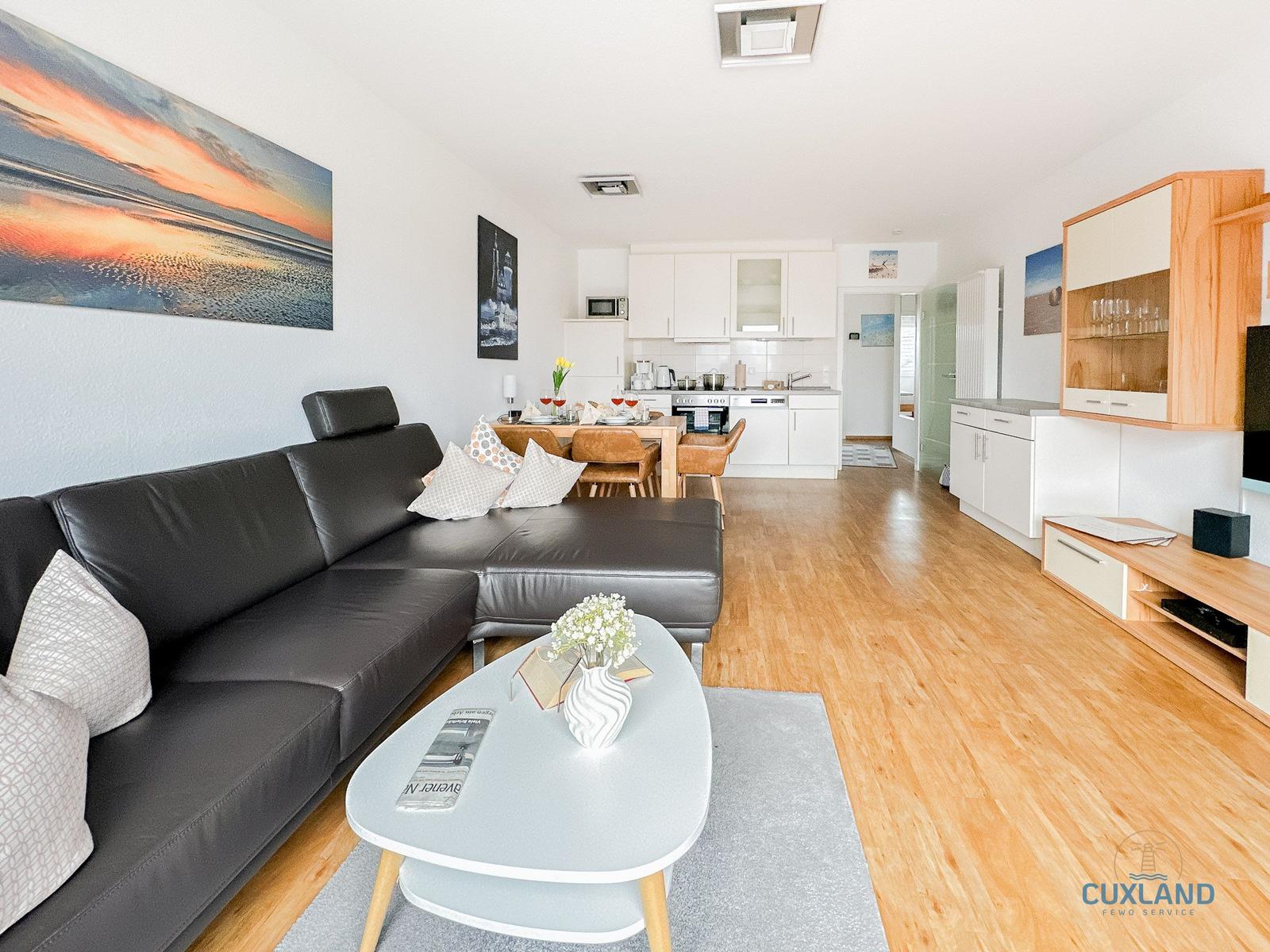 Wohnbereich mit Sofa, Esstisch und Küche im Hintergrund.