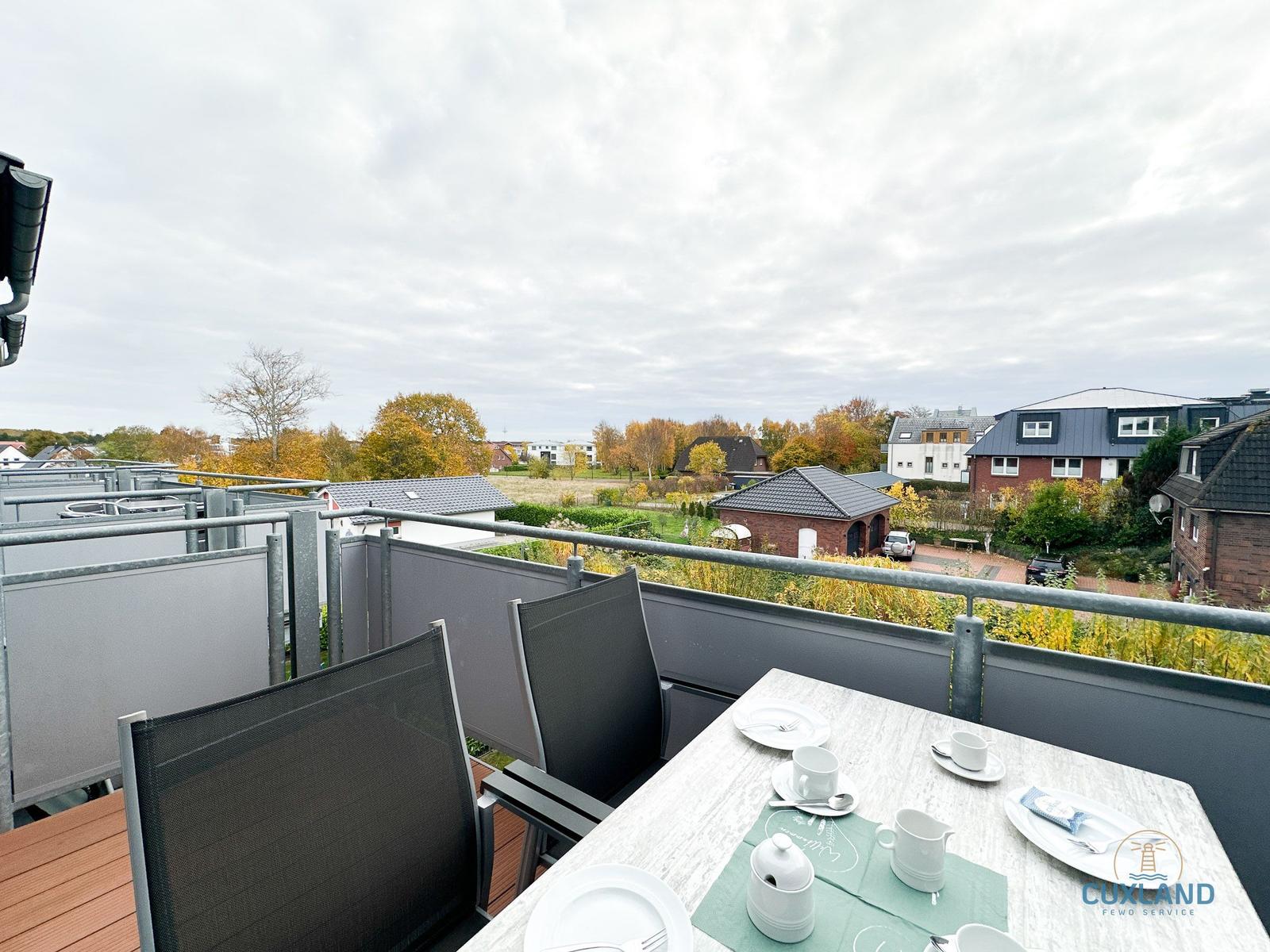 Terrasse mit Tisch und Stühlen, Blick auf Wohnhäuser und Bäume.