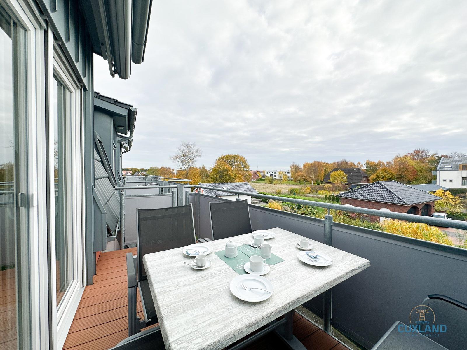 Terrasse mit Tisch und Stühlen, Blick auf Wohngebiet und Bäume.