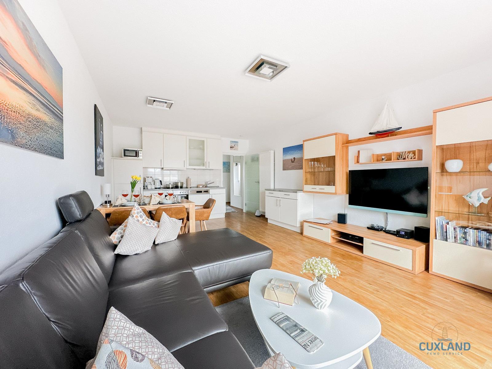 Wohnzimmer mit Sofa, TV und Küche im Hintergrund.