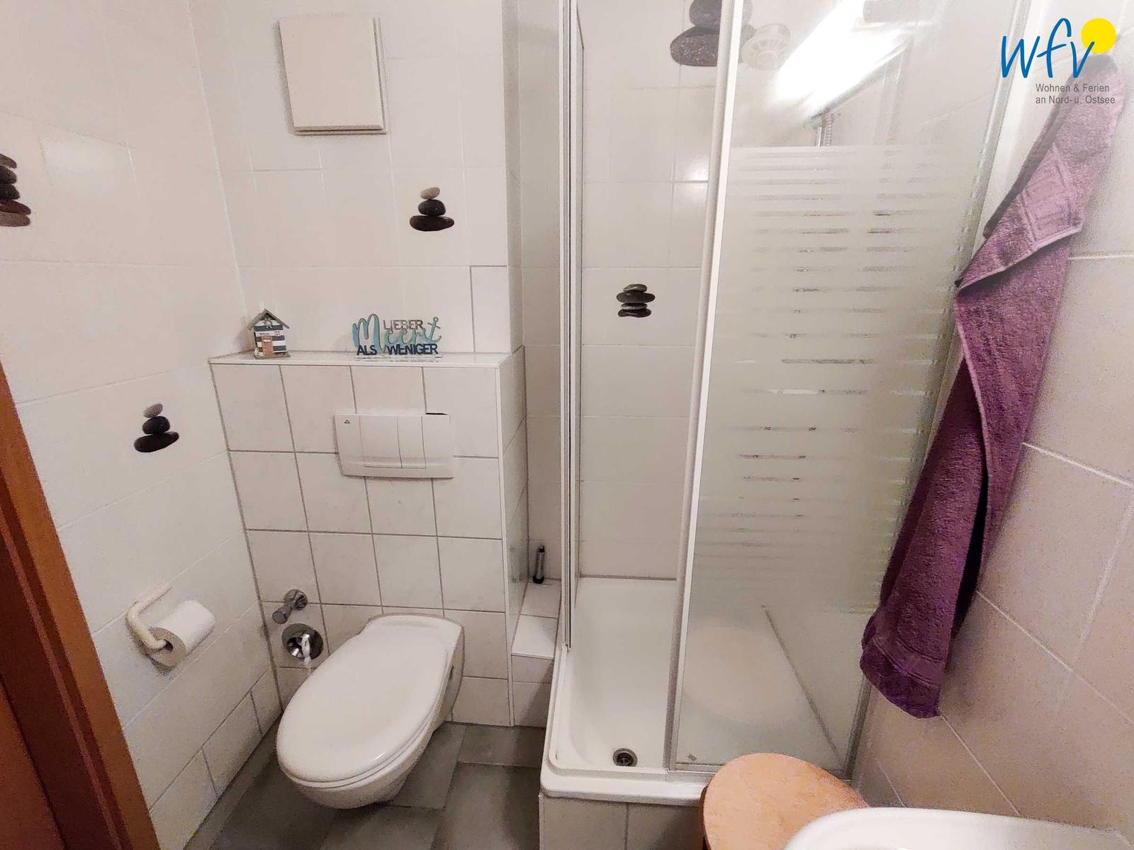 Badezimmer mit Dusche, Toilette und Waschbecken. Wanddekoration mit Steinen und einem Schild.