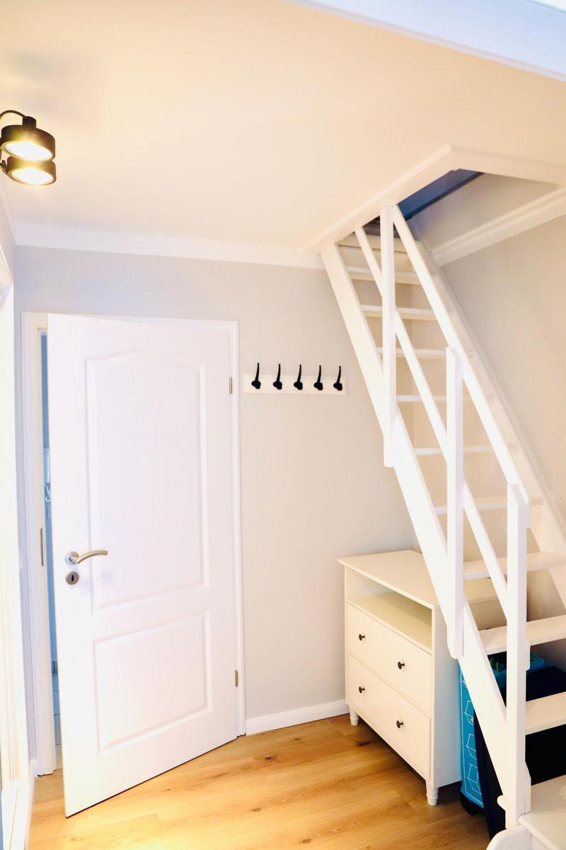 Hausgang mit weißen Treppe, Kleiderhaken und Schrank. Holzboden und weiße Tür.