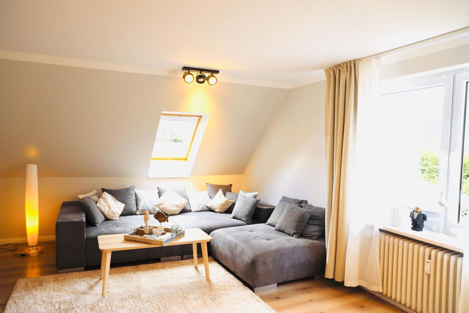 Wohnzimmer mit grauem Sofa, Holztisch und Dachfenster.