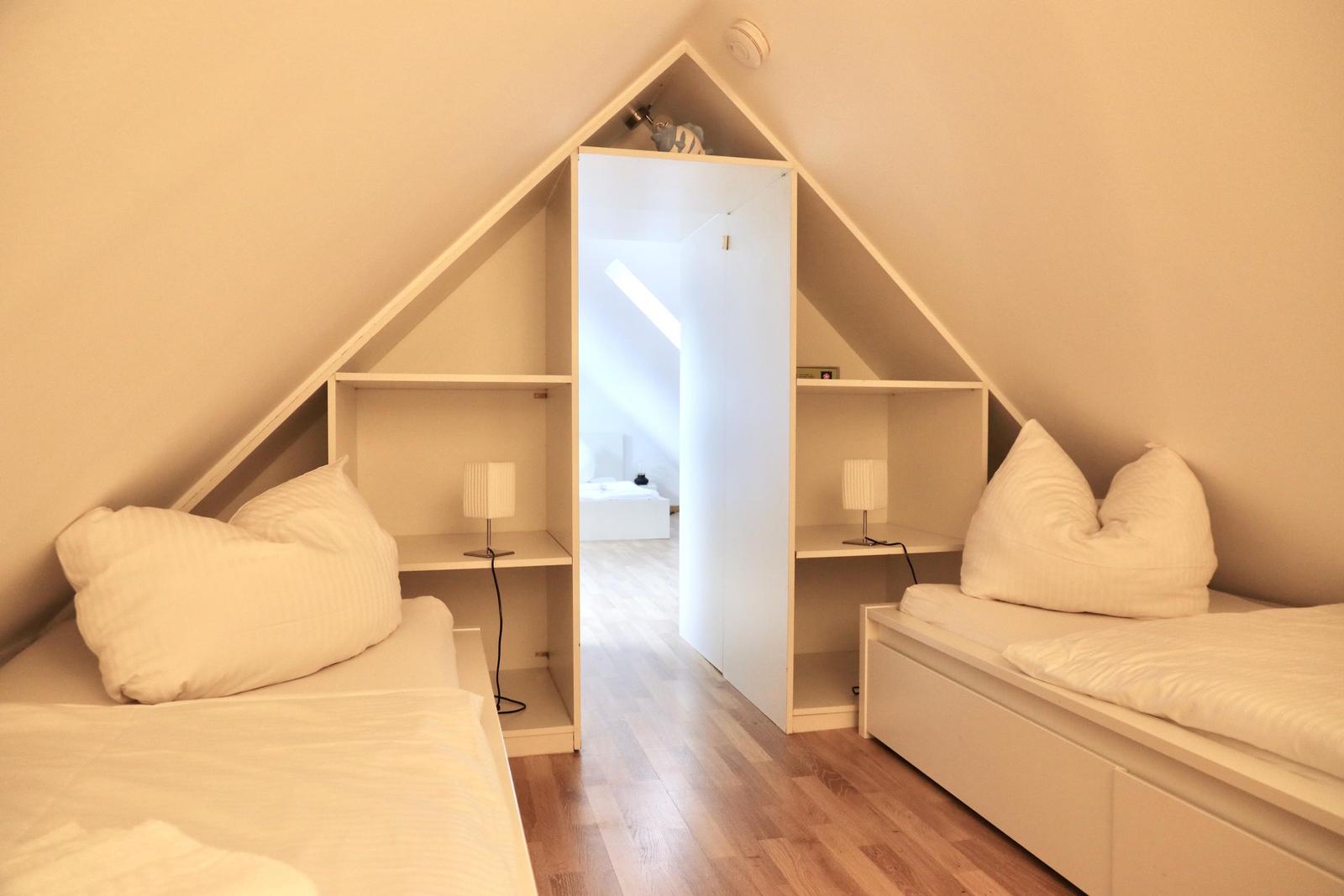 Zwei Betten unter Dachschrägen mit Nachttischen und Schränken