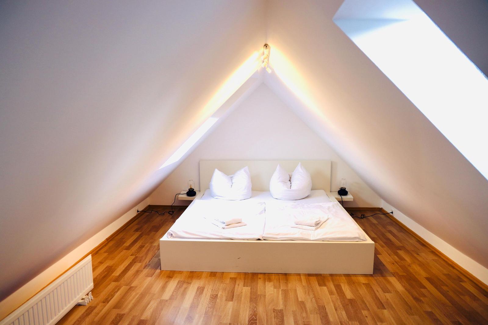 Schlafzimmer mit Dachschrägen, weißem Bett und Holzboden.