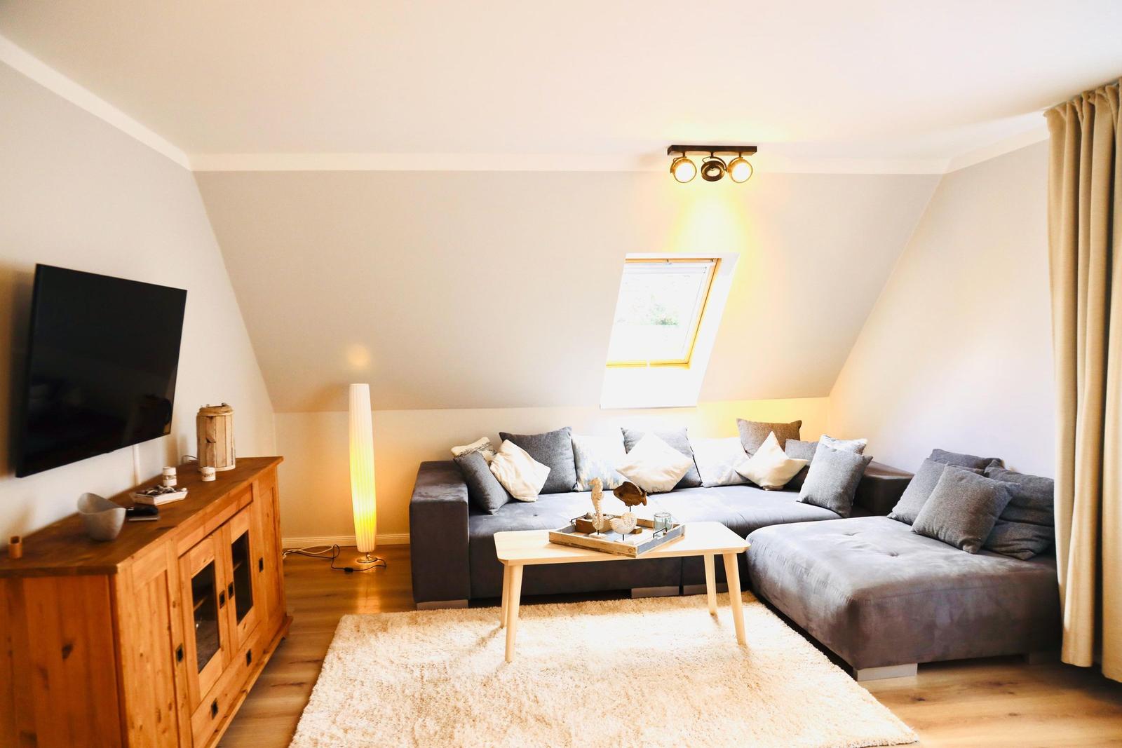 Wohnzimmer mit grauem Sofa, Holzmöbeln und Dachfenster.