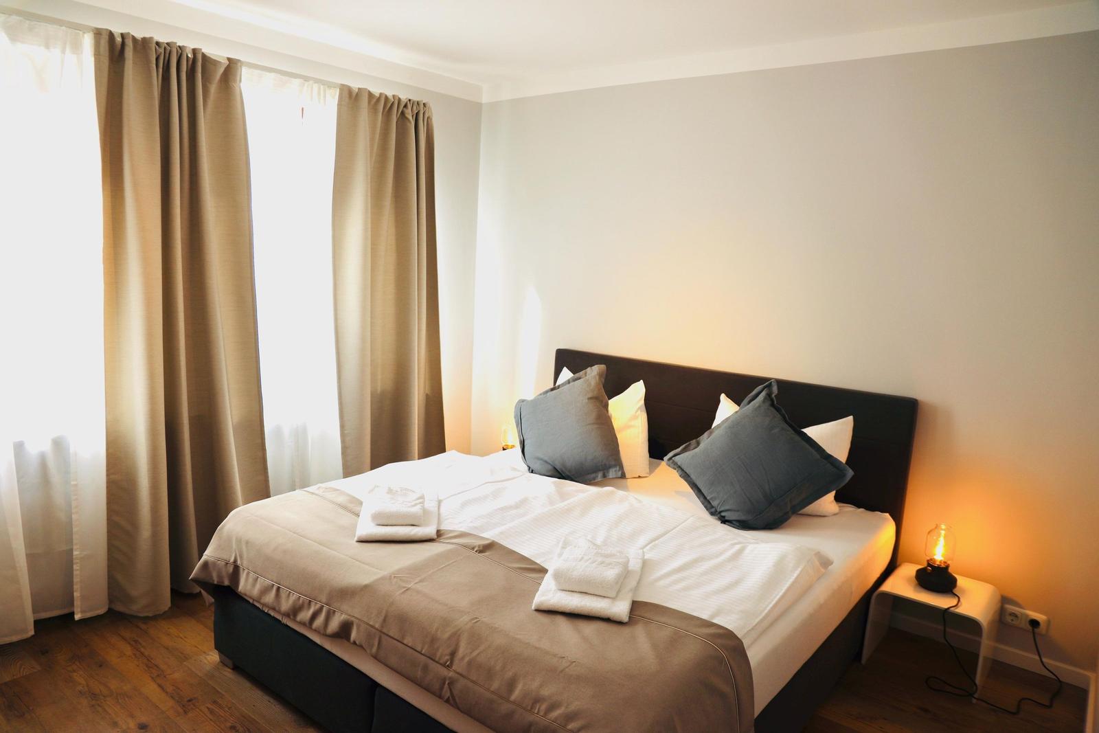 Schlafzimmer mit Bett, Vorhängen und Nachttisch mit Lampe.