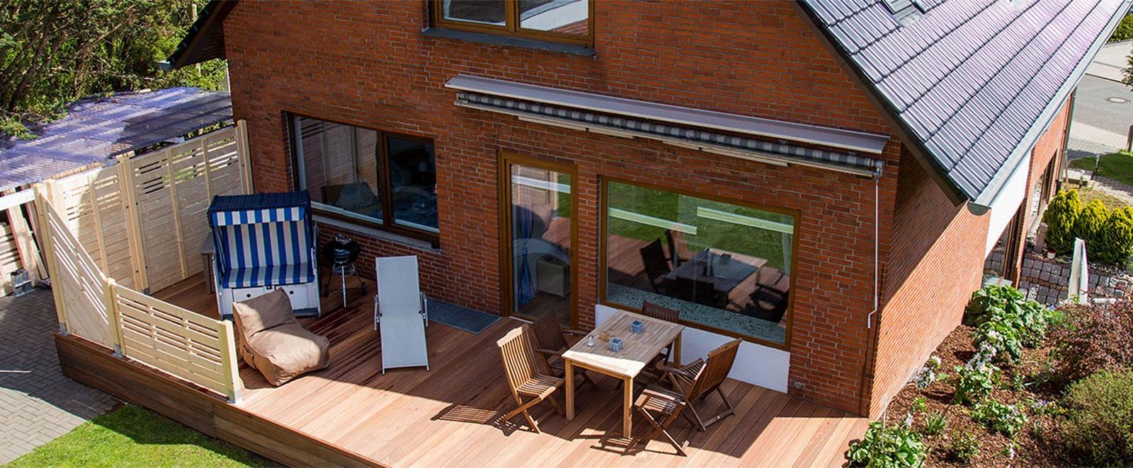 Holzterrasse mit Sitzgruppe und Strandkorb vor Backsteinhaus.