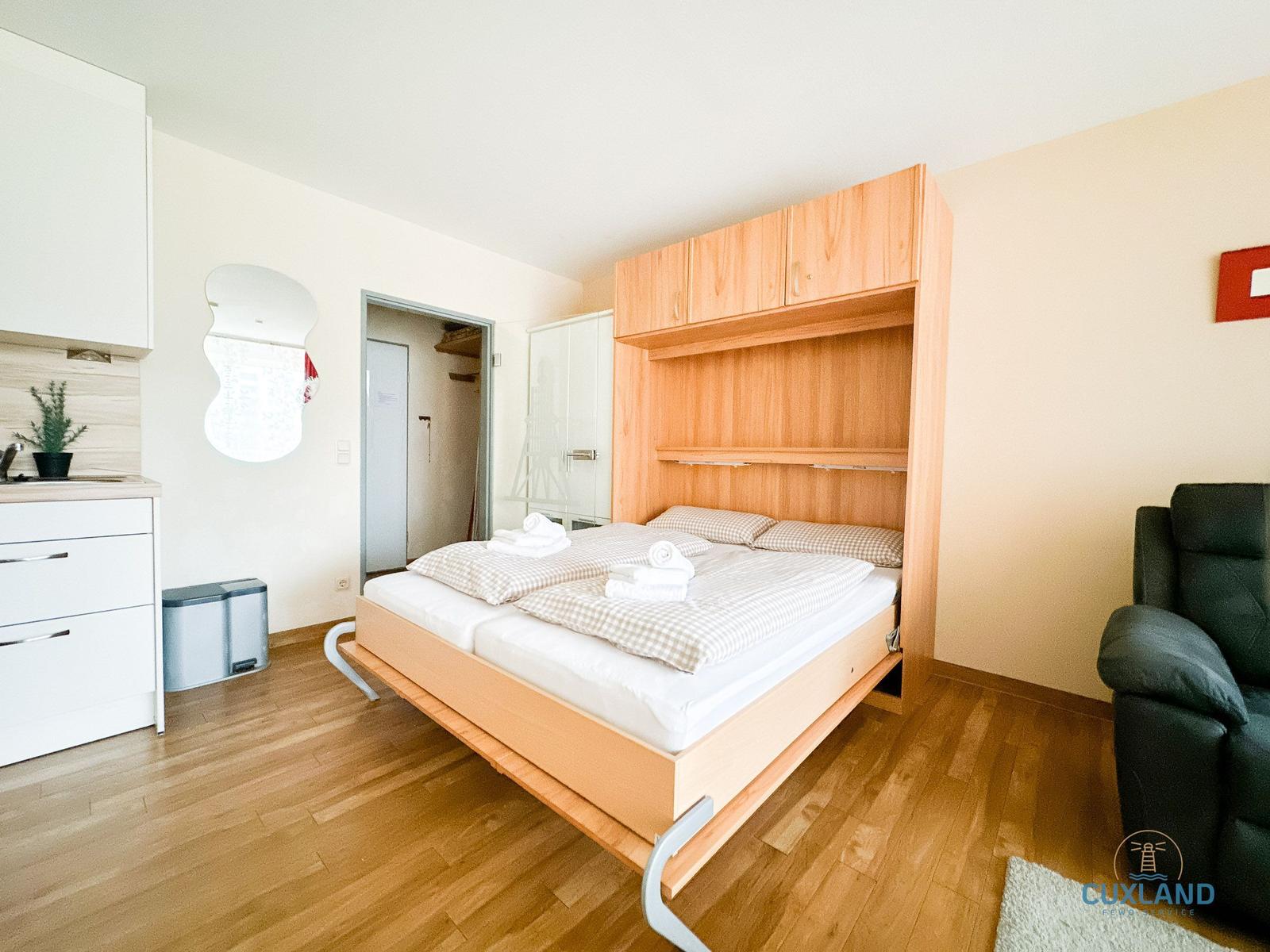 Schlafzimmer mit Bett, Küchenzeile und Sessel.