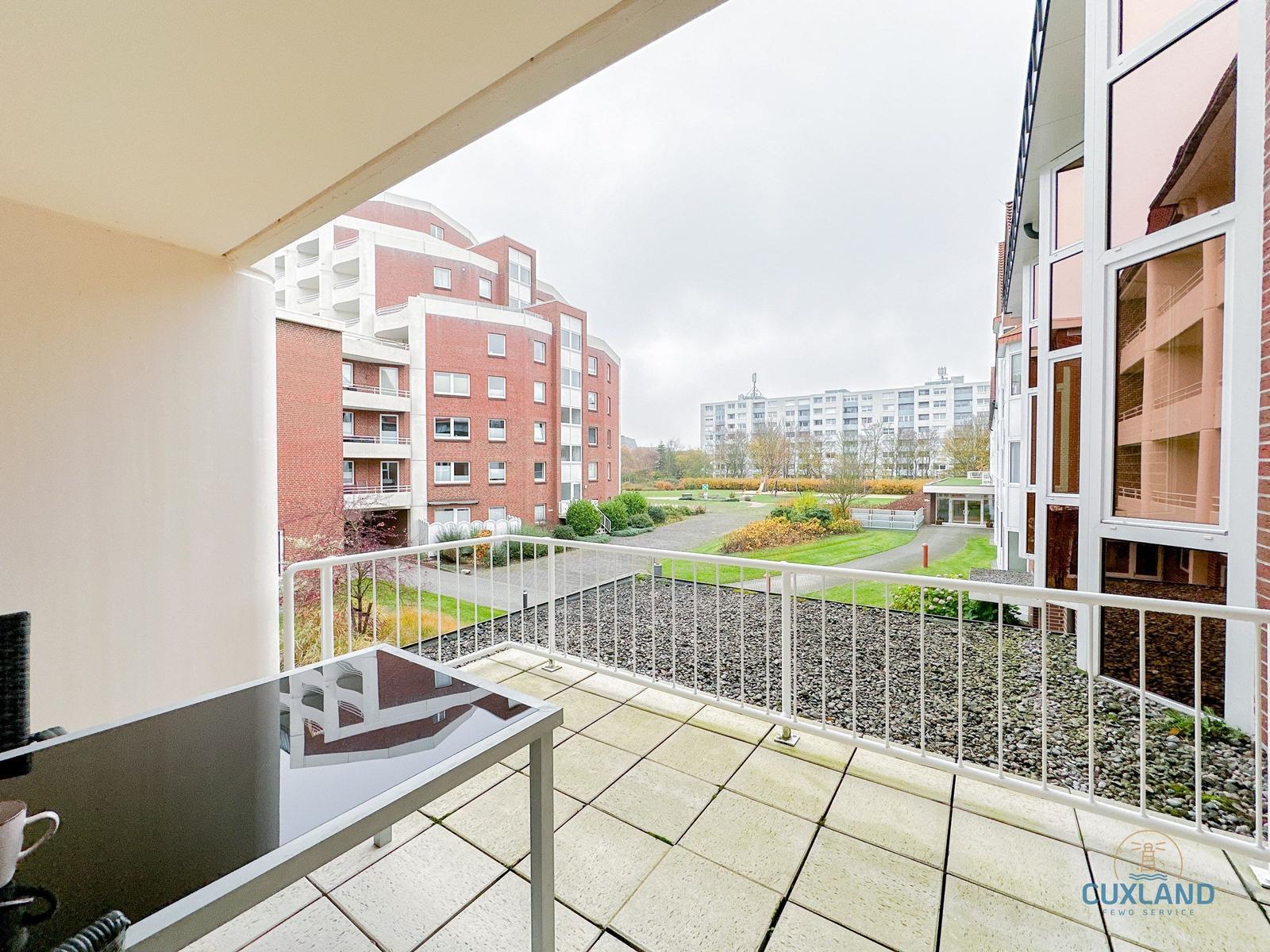 Terrasse mit Tisch und Blick auf Wohnkomplex und Grünflächen.