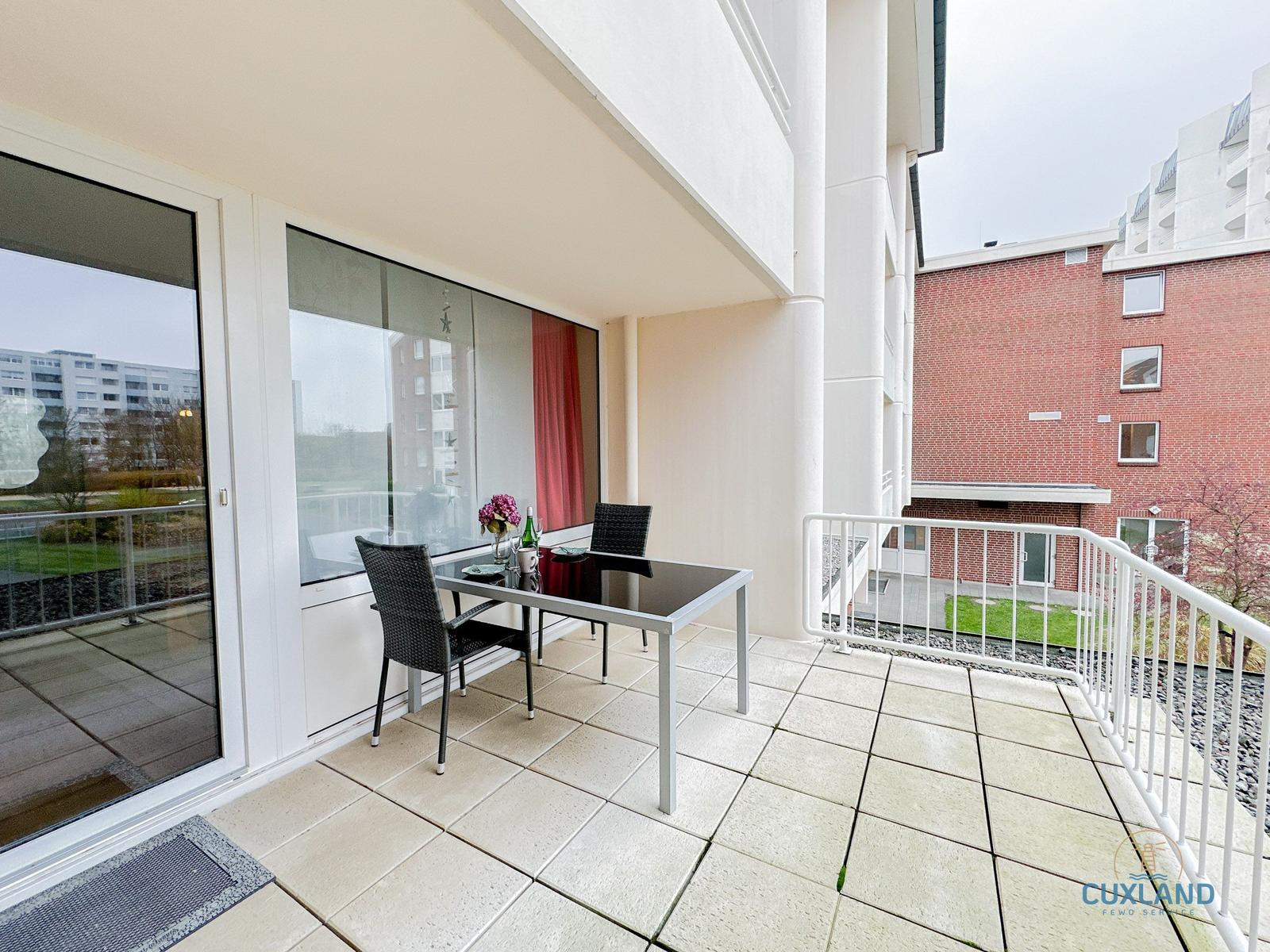 Terrasse mit Tisch und Stühlen, Blick auf Gebäude und Grünflächen.