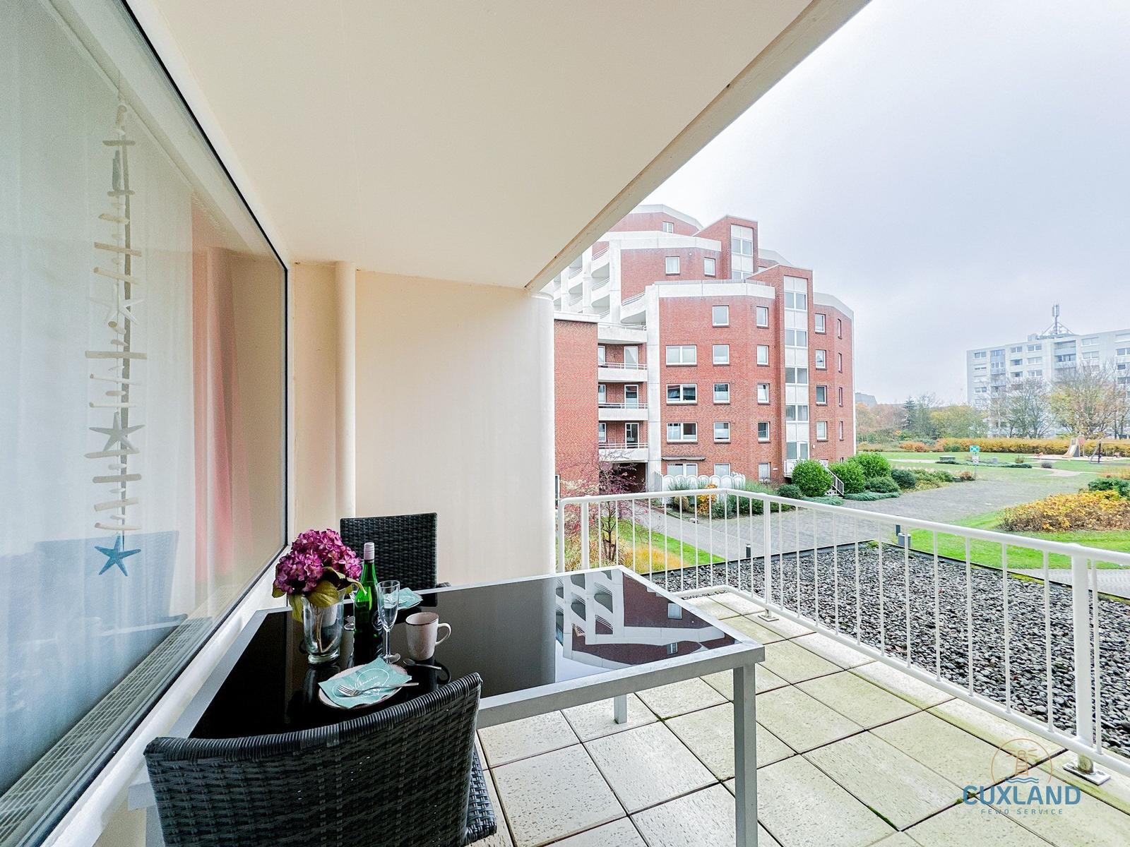 Terrasse mit Tisch und Stühlen, Blick auf Wohngebäude und Grünfläche.