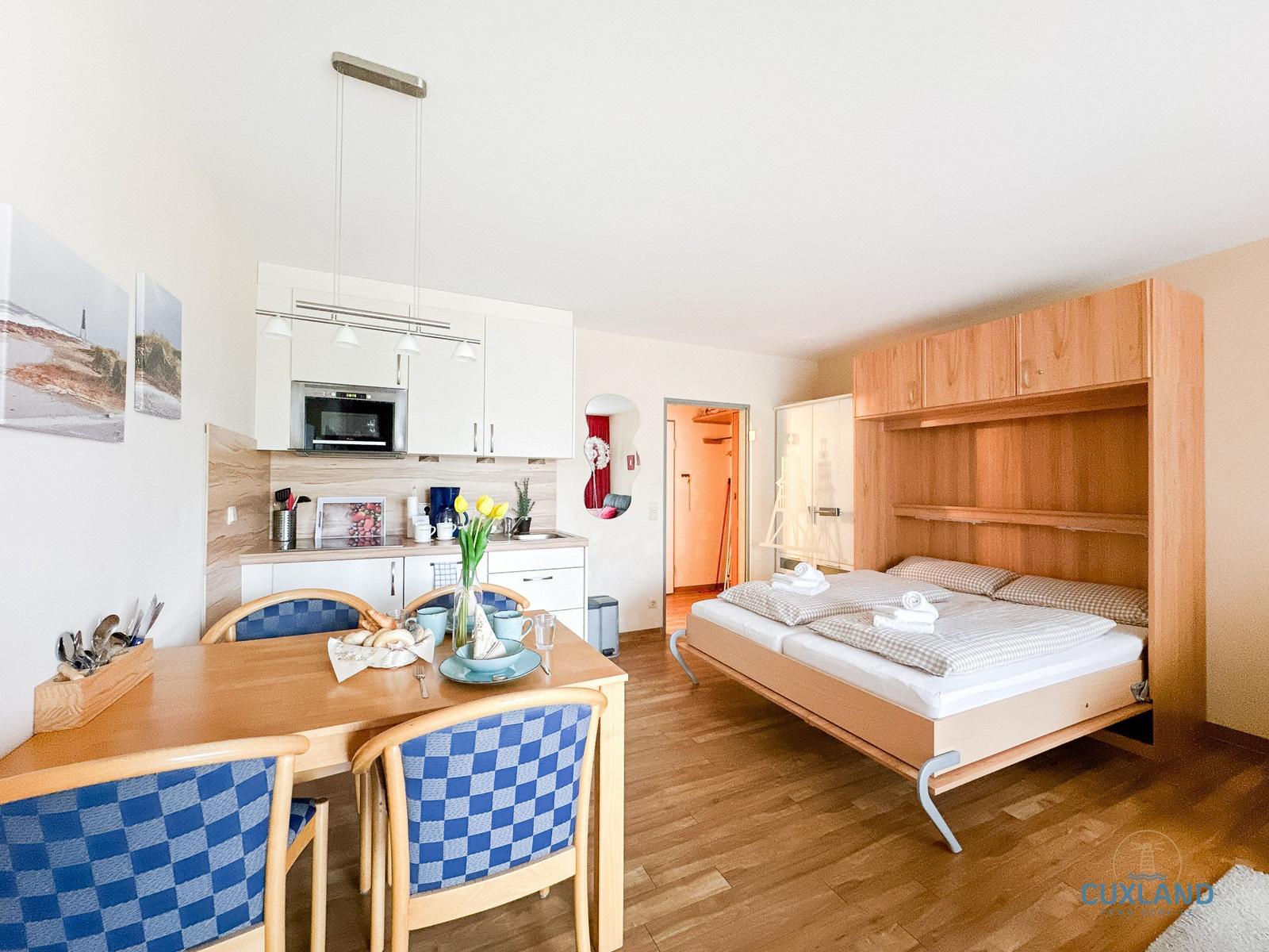 Schlafzimmer mit Bett, Küchenbereich und Esstisch mit Stühlen.