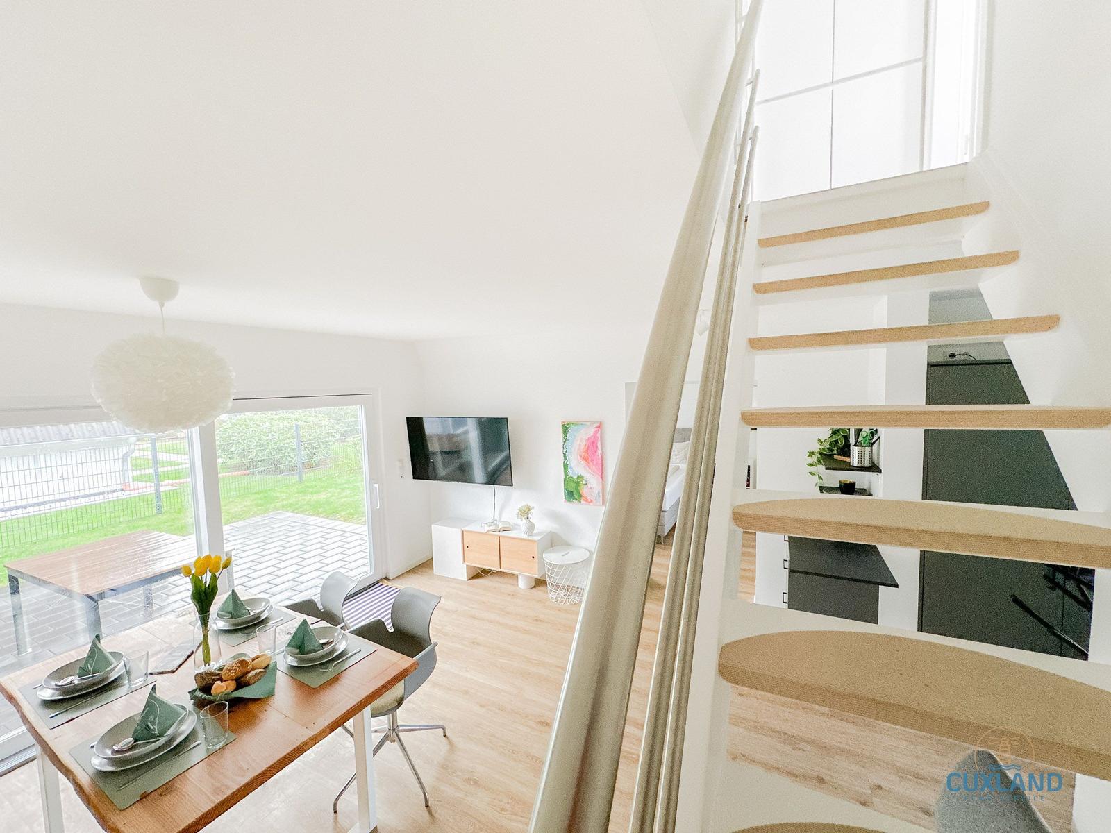 Essbereich mit Tisch, Stühlen und Blick auf Terrasse. Treppenhaus führt zur oberen Etage.