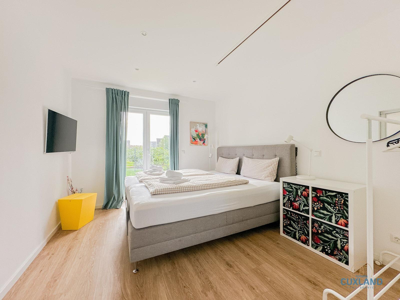 Schlafzimmer mit Bett, TV und Fenster mit Blick auf Garten.