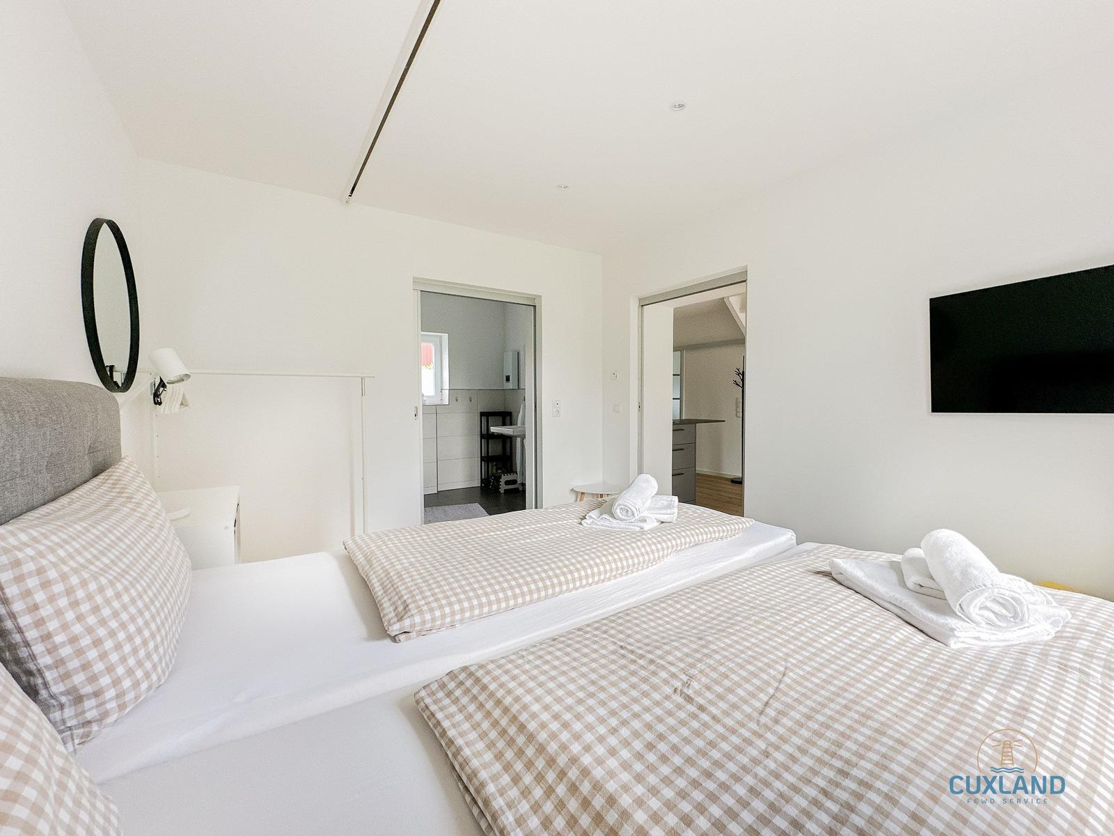 Zwei Betten mit karierten Bettwäsche, Spiegel und Fernseher an der Wand.