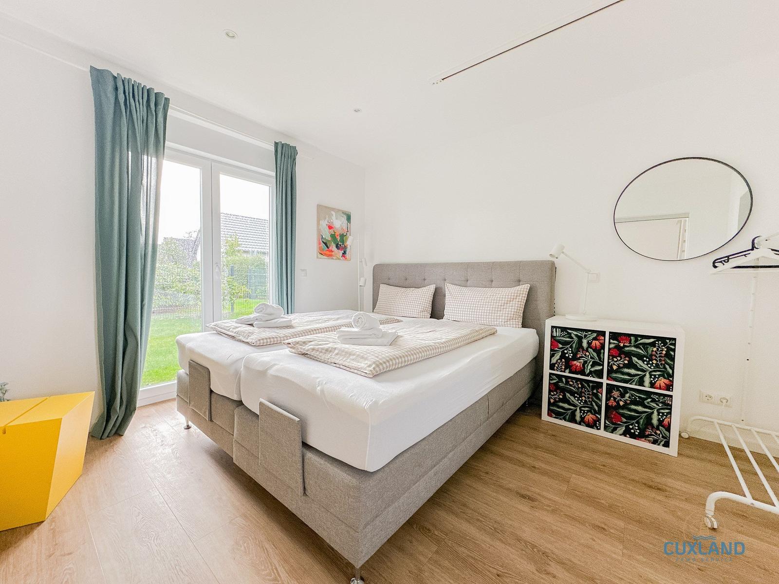 Schlafzimmer mit Doppelbett, Fenster, Schrank und Spiegel.