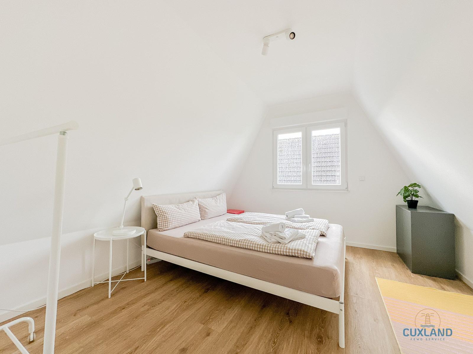 Schlafzimmer mit Doppelbett, Fenster und Holzboden.