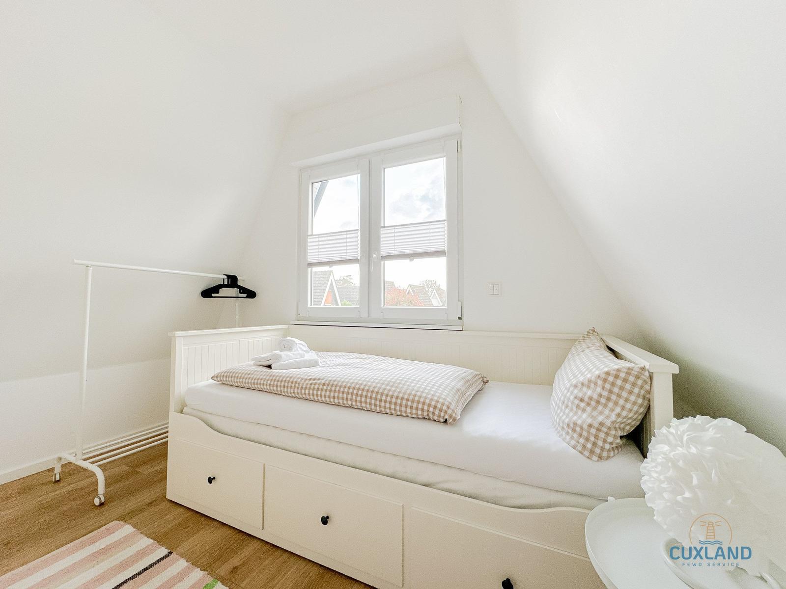 Schlafzimmer mit weißem Bett, Fenster und Kleiderständer.