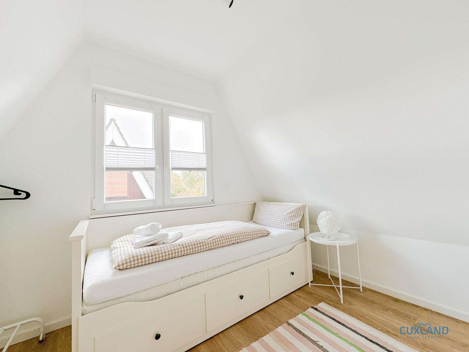 Schlafzimmer mit Bett, Fenster und kleinem Tisch.