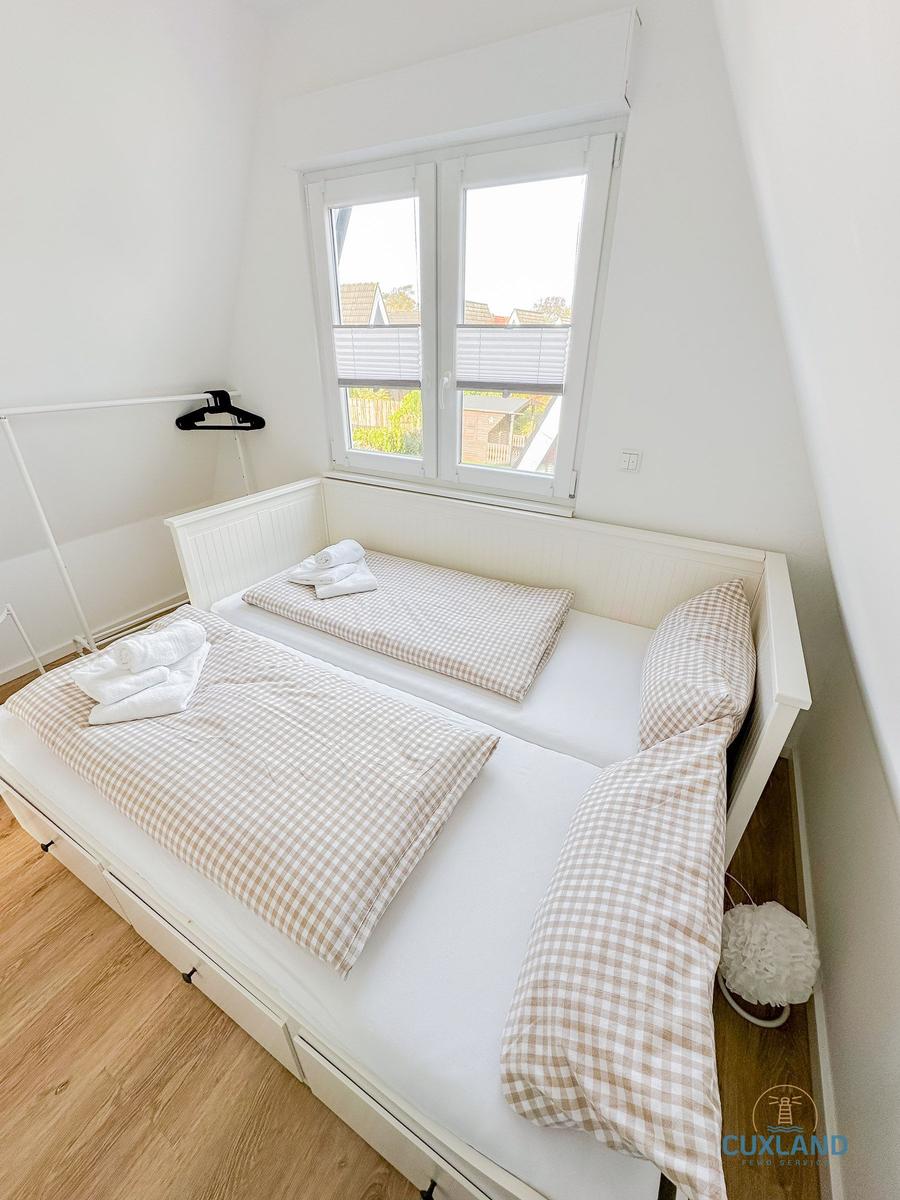 Schlafzimmer mit zwei Betten und Fenster. Holzfußboden und weißer Schrank.