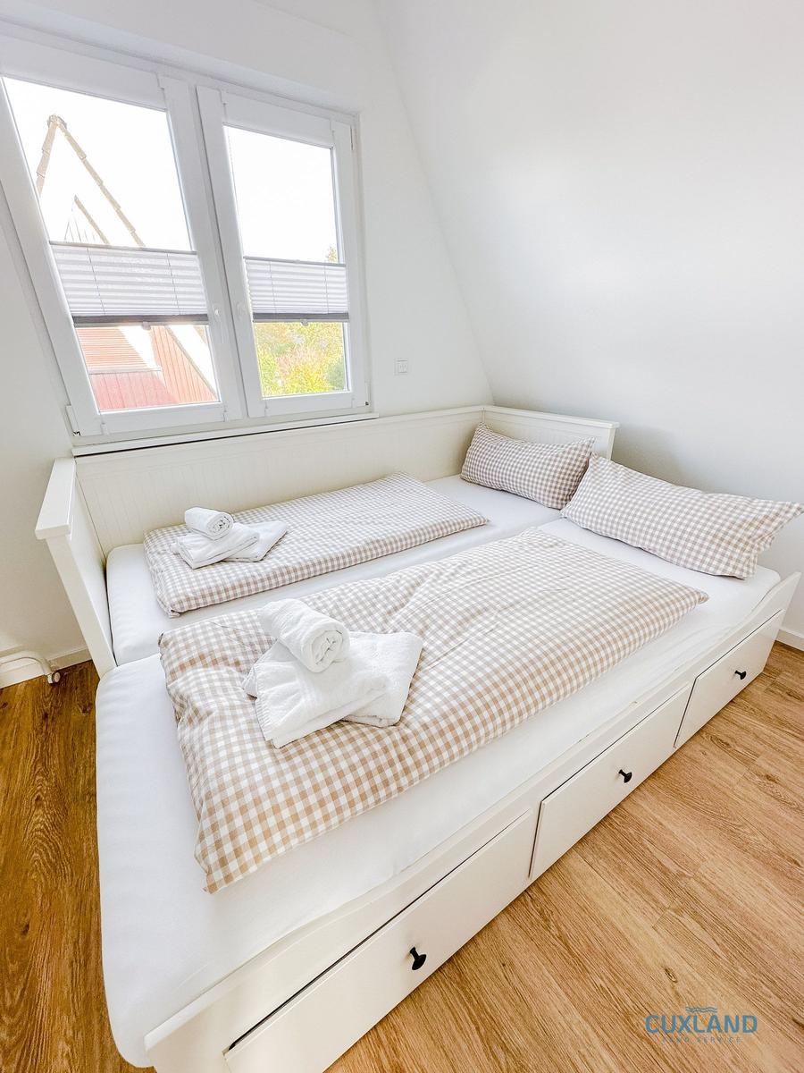 Zimmer mit Schlafcouch, Fenster und Holzboden.