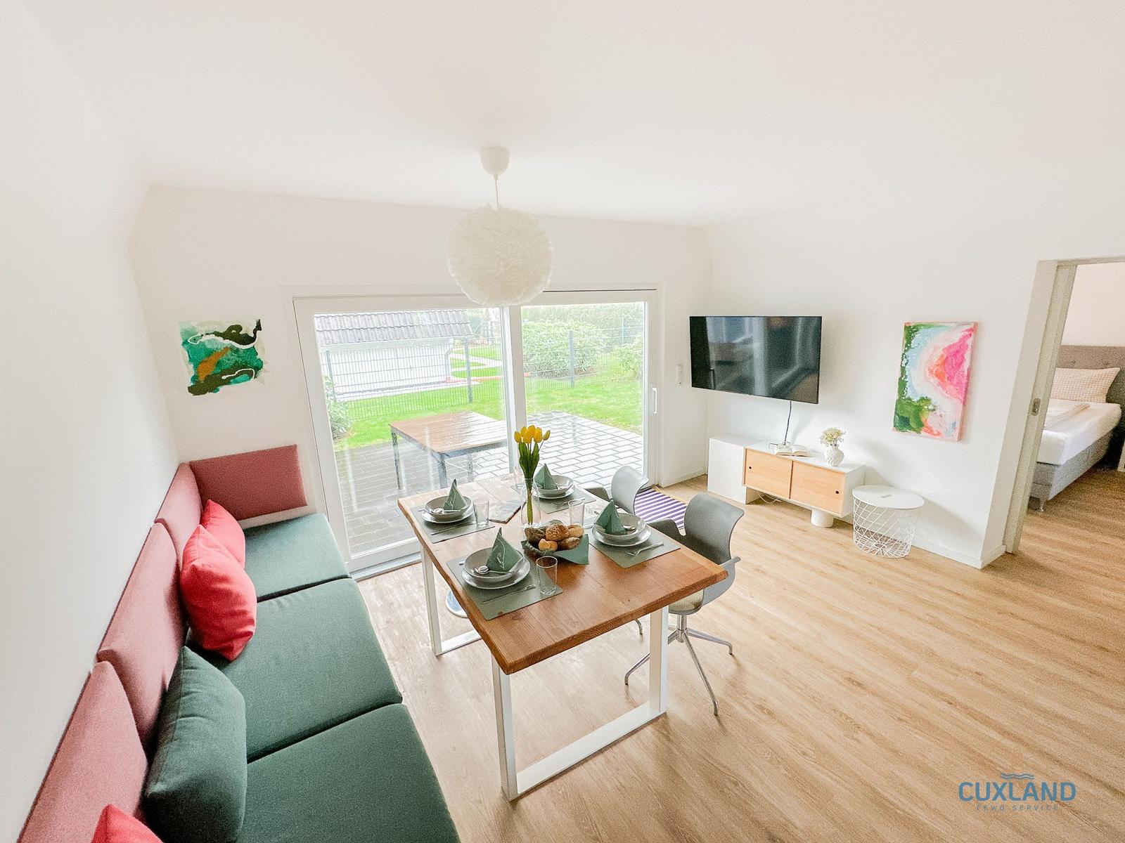 Wohn- und Essbereich mit Sofa, Tisch und TV. Durchgang zur Schlafzimmer.