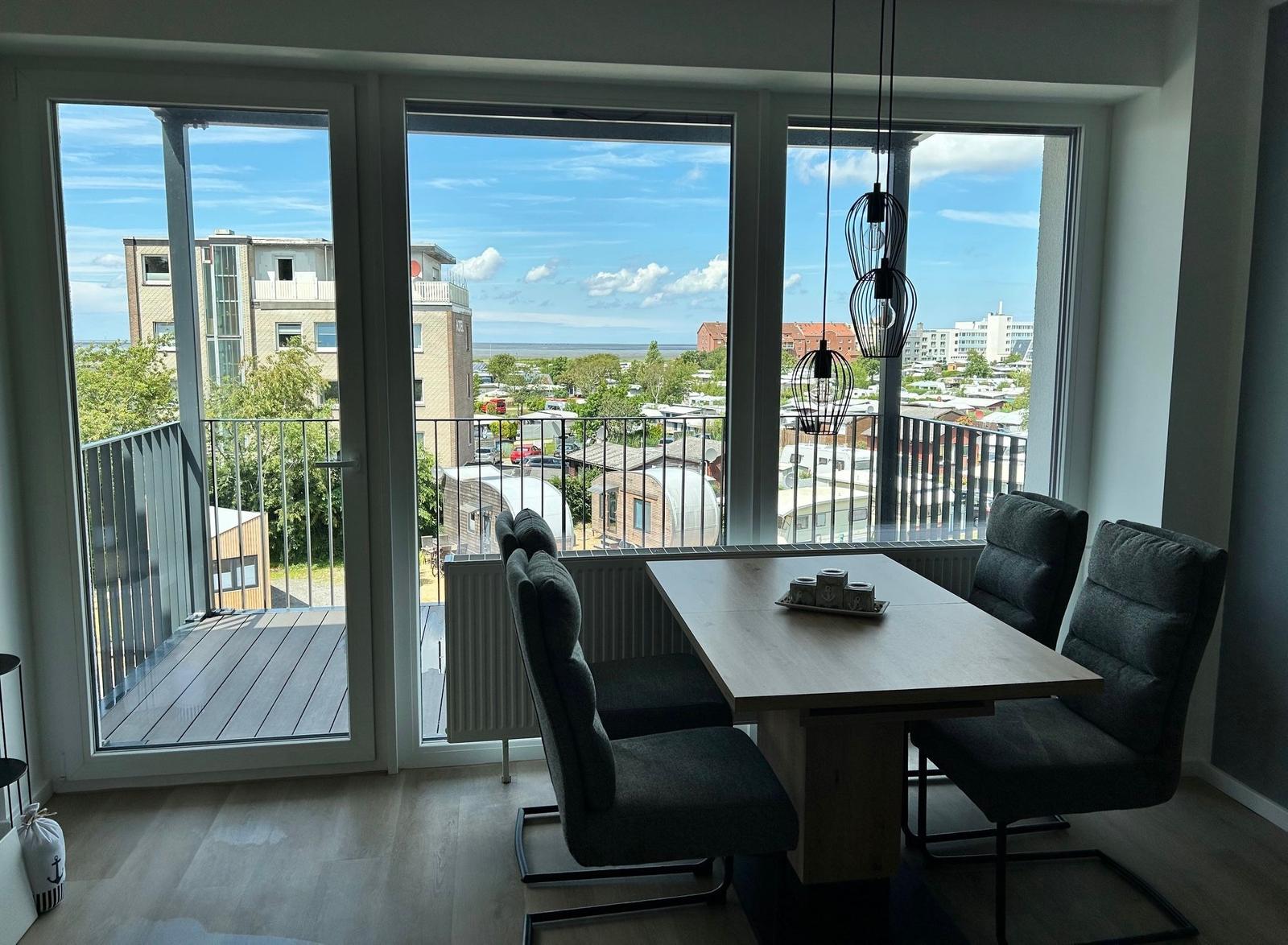 Essbereich mit Tisch und Stühlen. Große Fenster mit Blick auf Balkon und Stadt.
