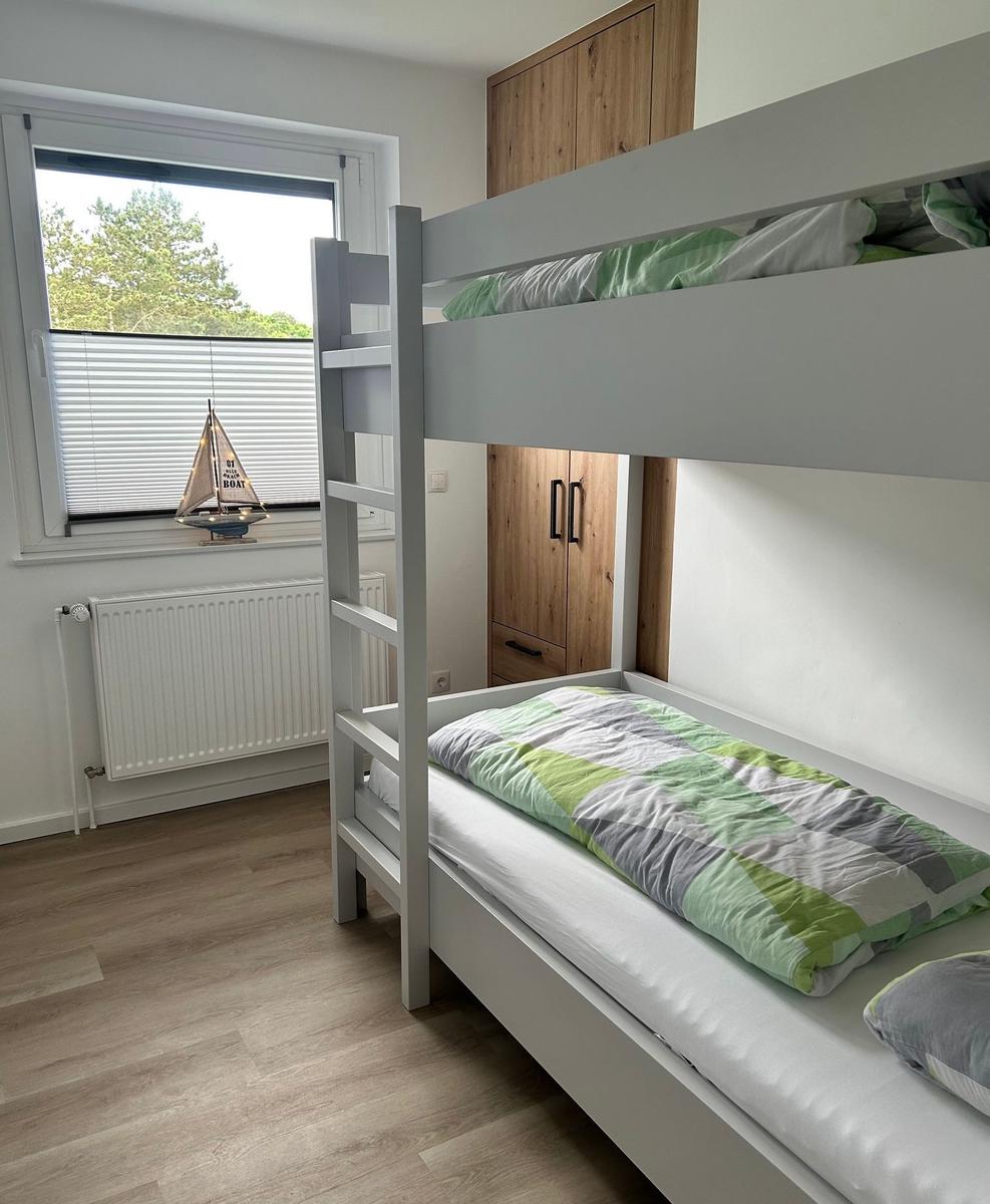 Zimmer mit Doppelstockbett, Fenster und Holzschrank.