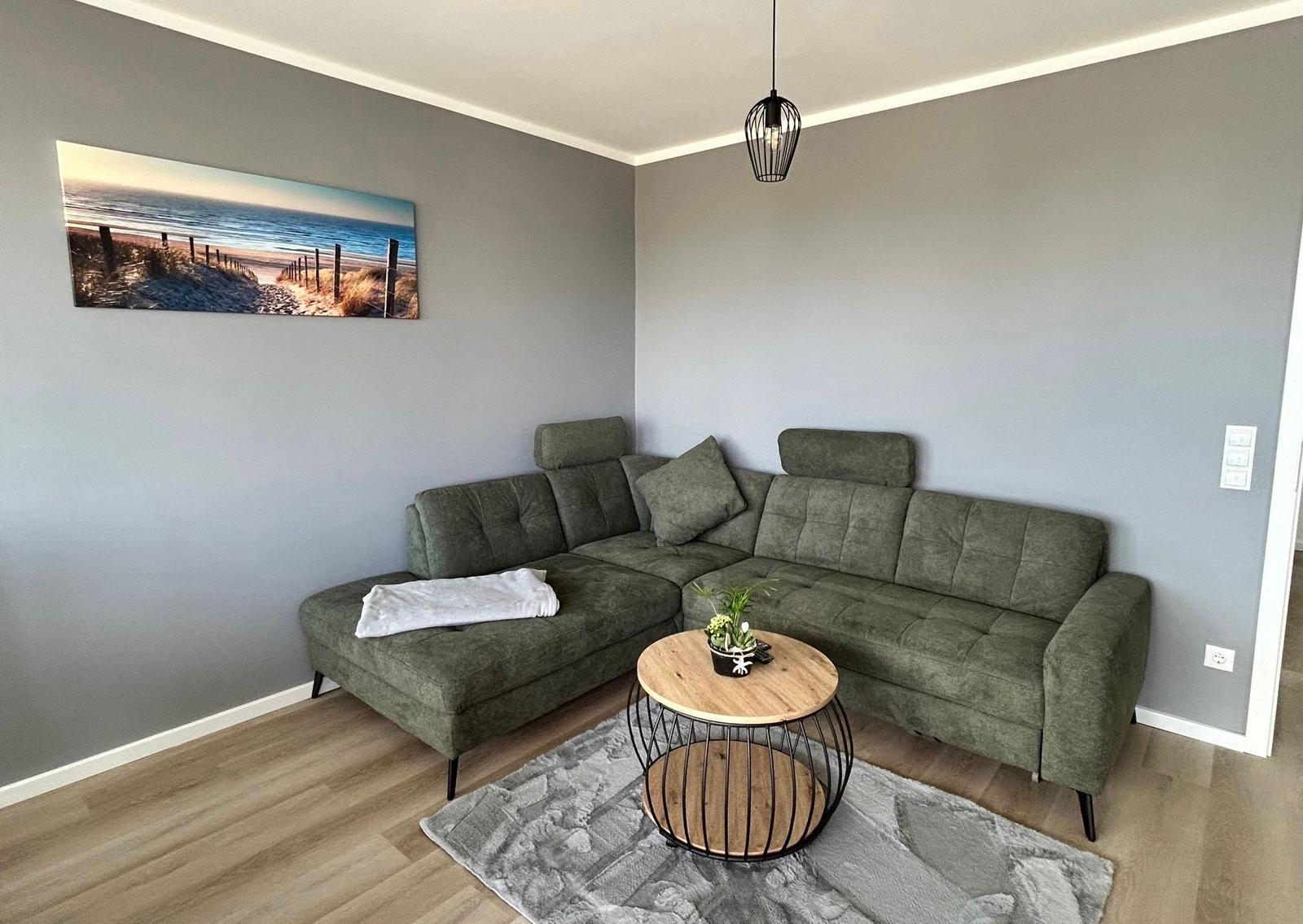 Ein Wohnzimmer mit grünem Sofa, runden Tisch und Wandbild.