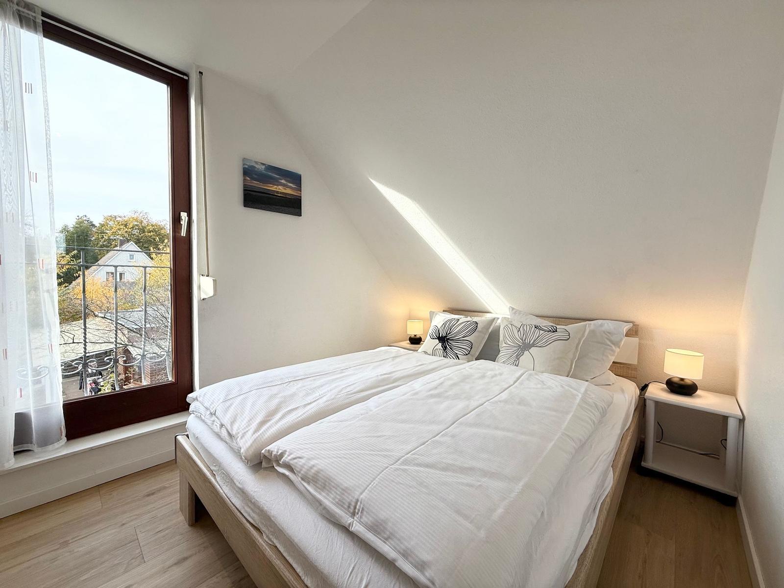 Bedroom with sloped ceiling, bed, nightstands, and window with view.
