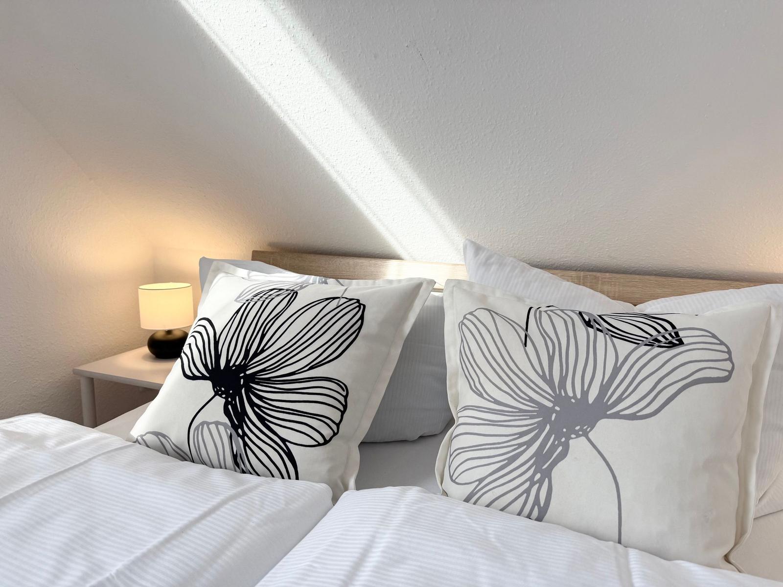 The bed has pillows and a duvet cover. A lamp is on a bedside table.