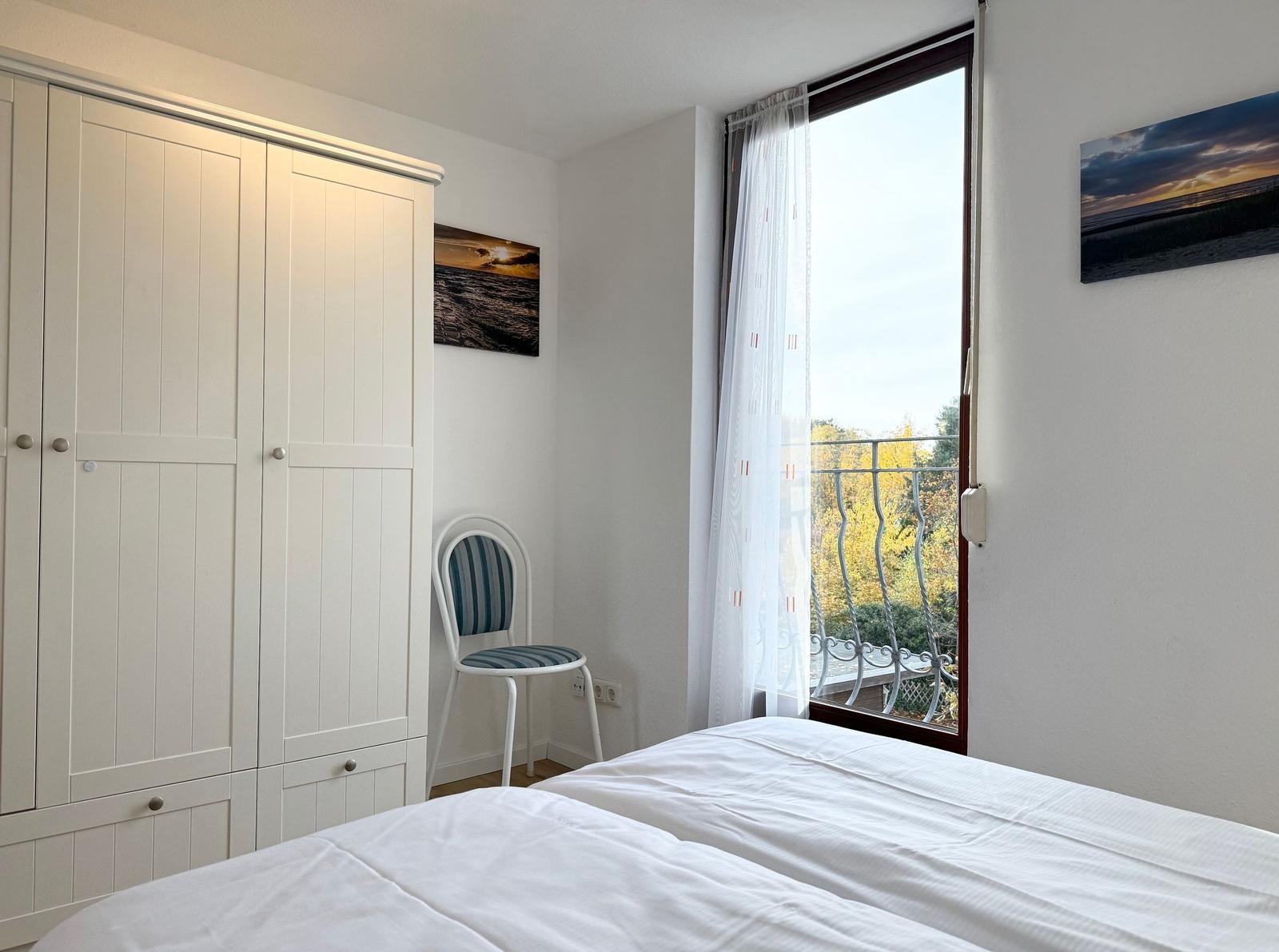 Bedroom with white wardrobe, chair, and balcony view.