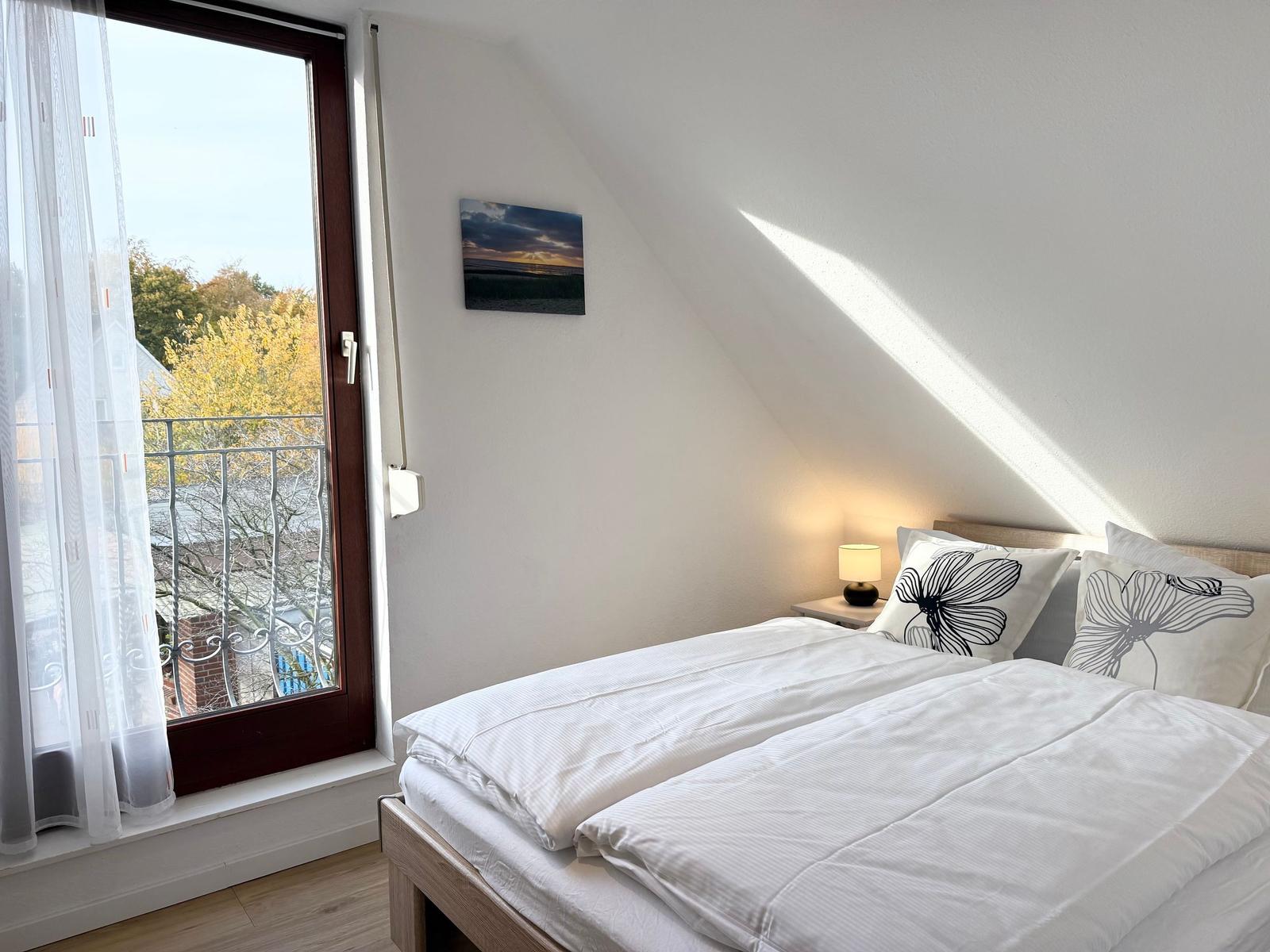 Bedroom with double bed, window to balcony, and wall picture.