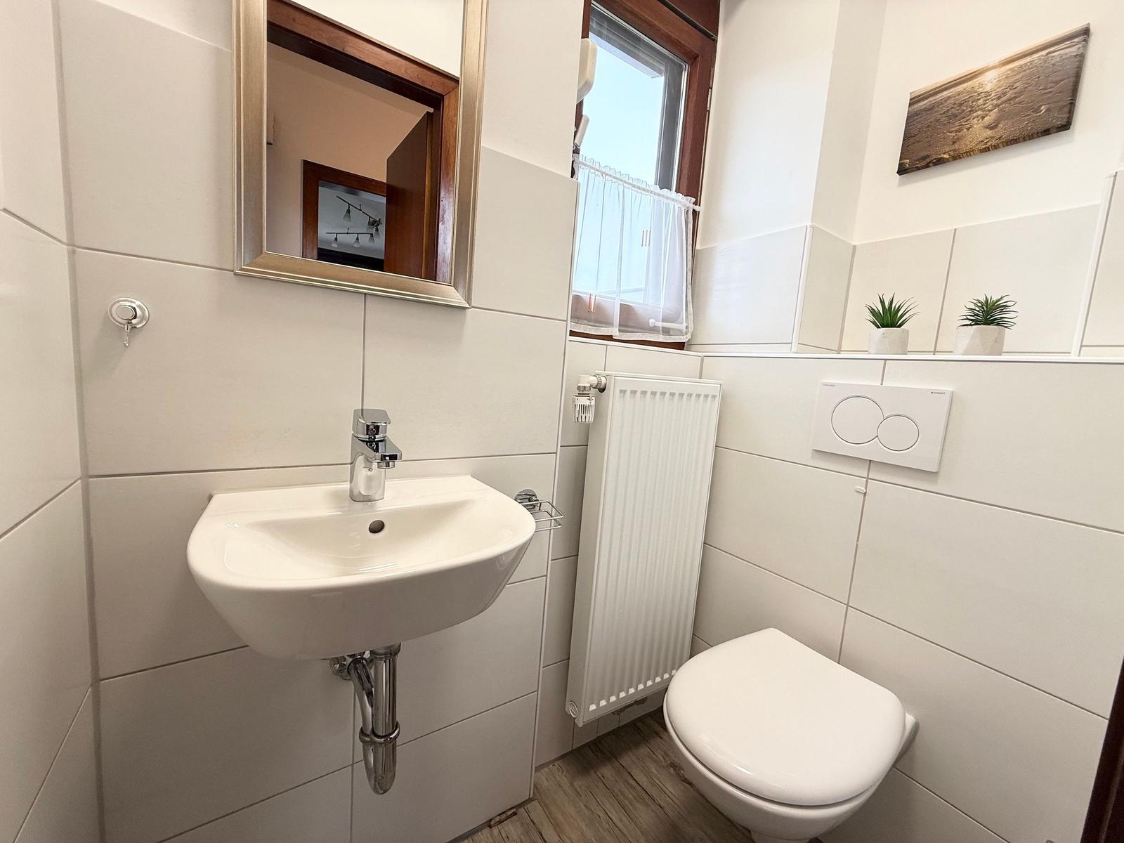 Bathroom with sink, mirror, toilet, and window.