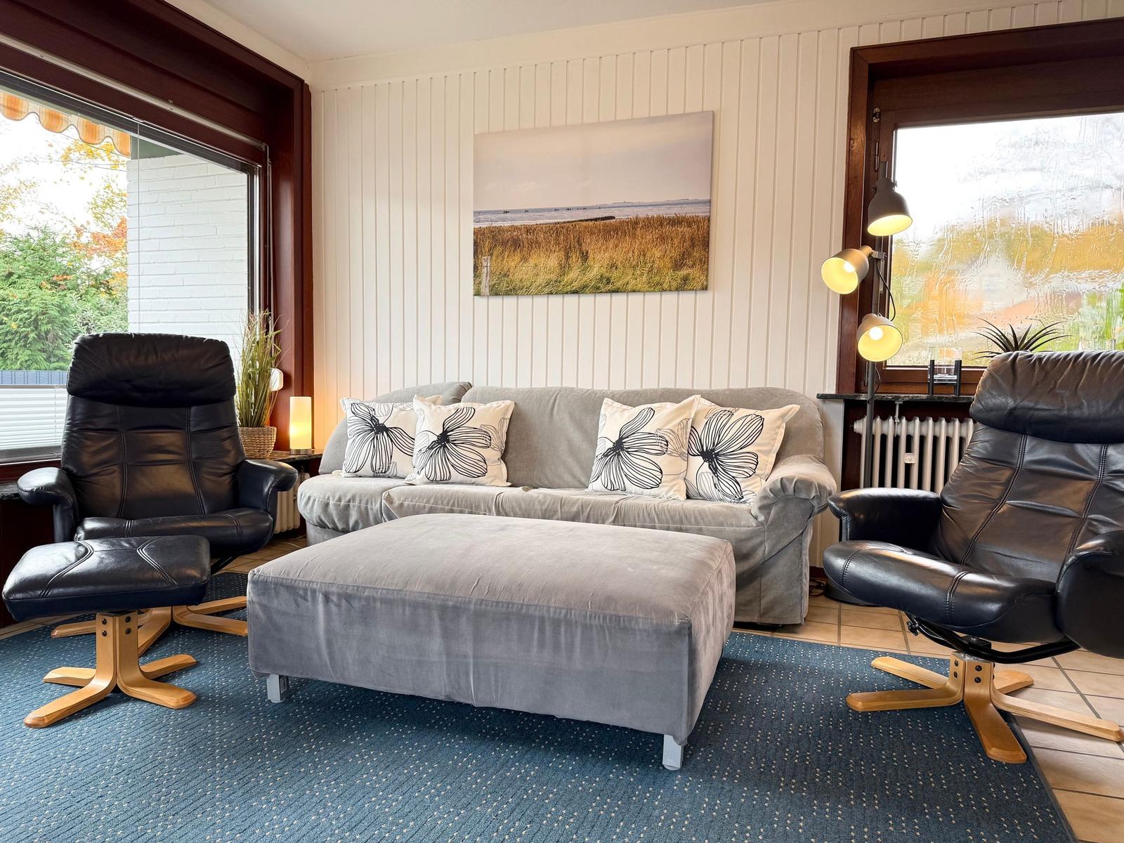 A living room with a gray sofa, two black chairs, and a wall picture.