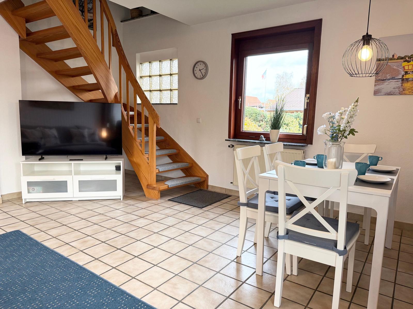 Living and dining area with wooden stairs, TV, and table with chairs.