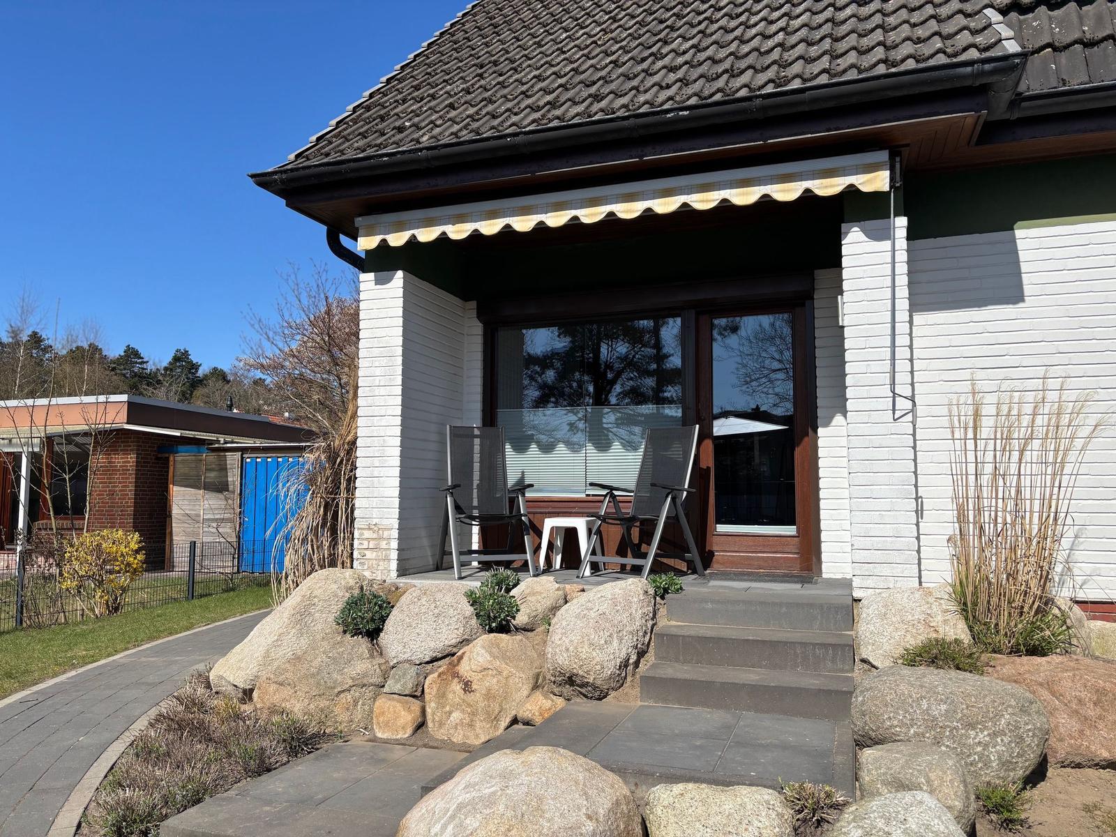 House with terrace, seating area, and stone beds in the front garden.