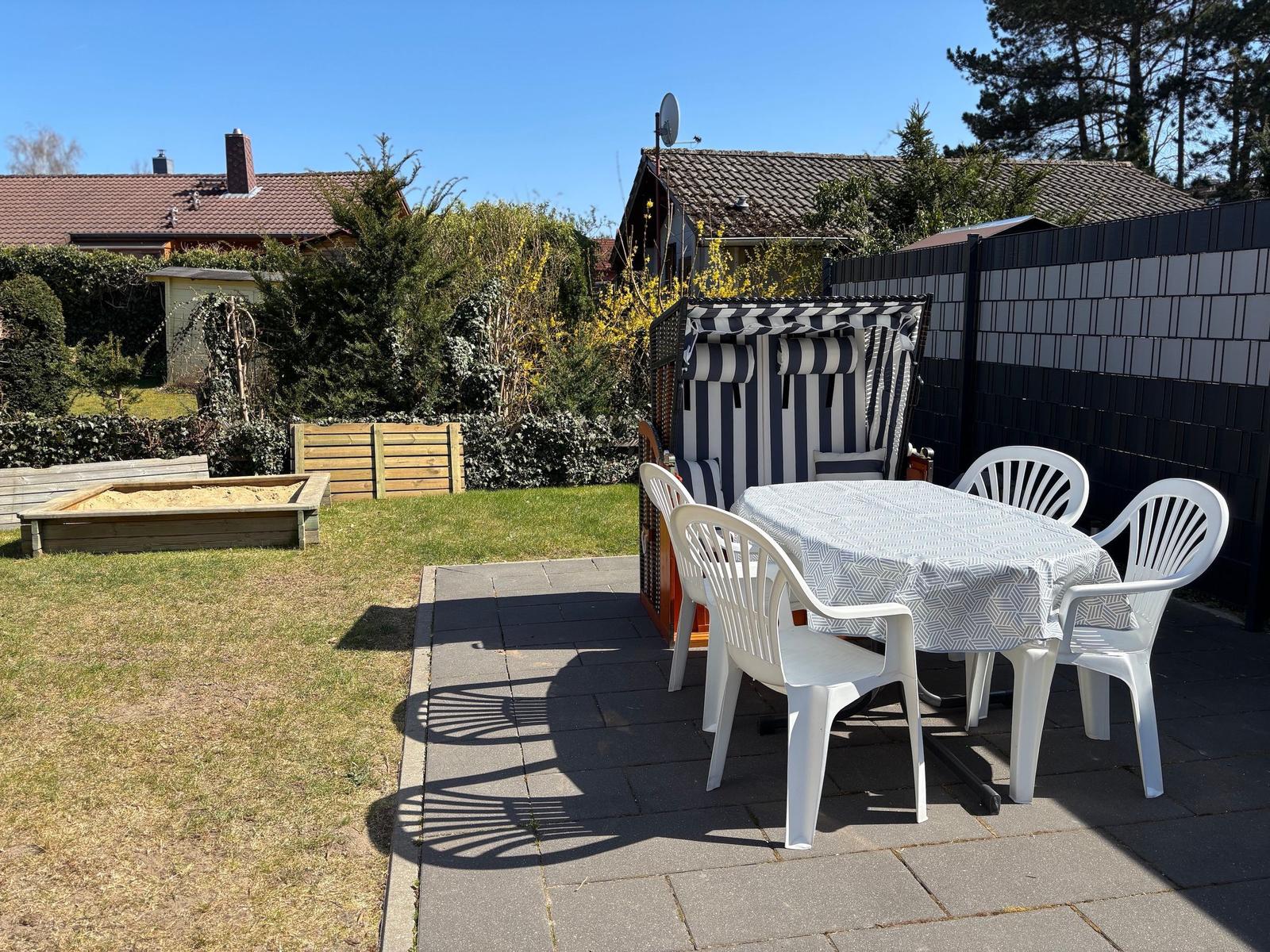 Backyard with table, chairs, and beach chair. Garden area with sandbox and fence.