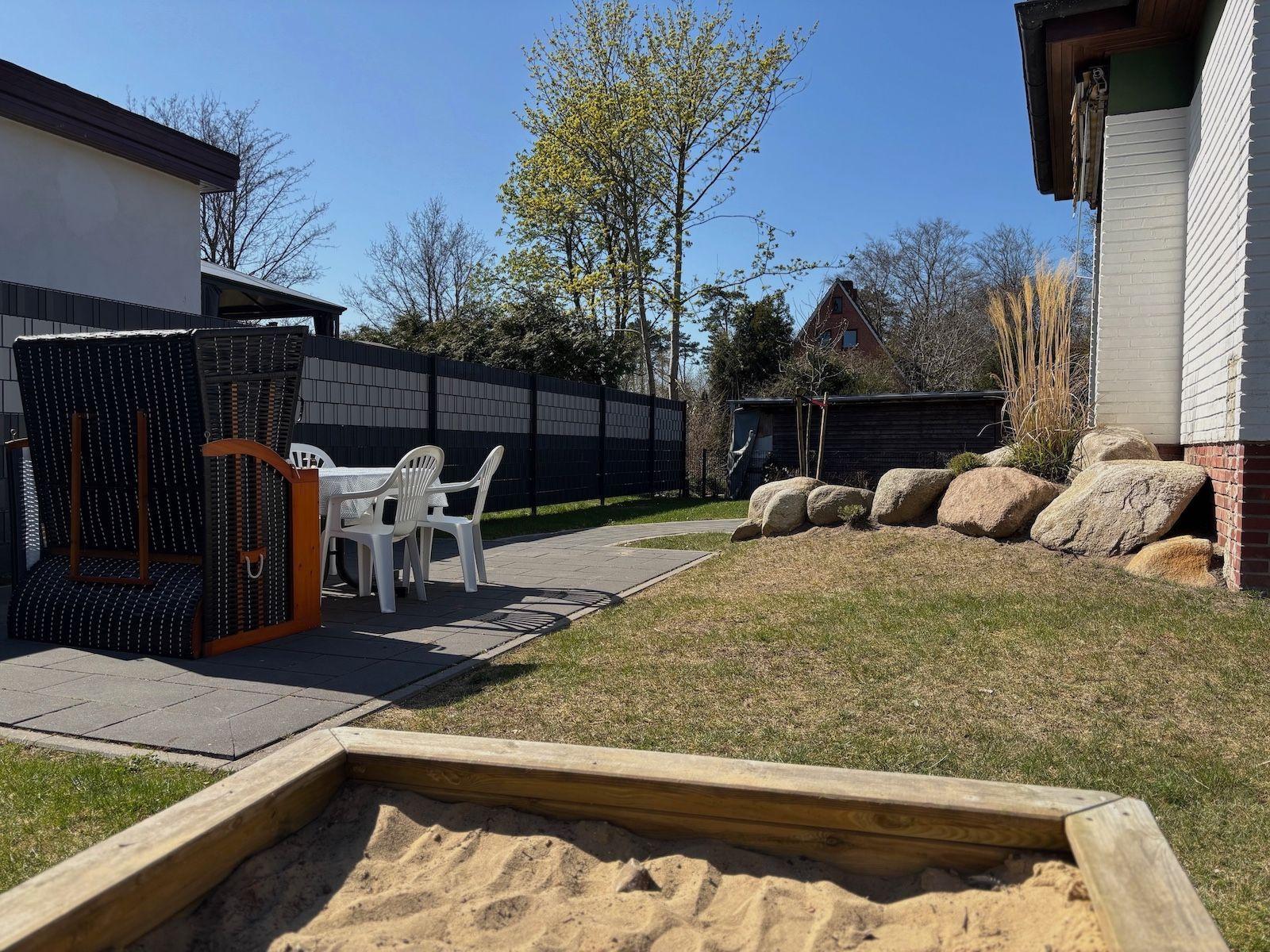 Backyard with sandbox, patio, lawn, and rocks.
