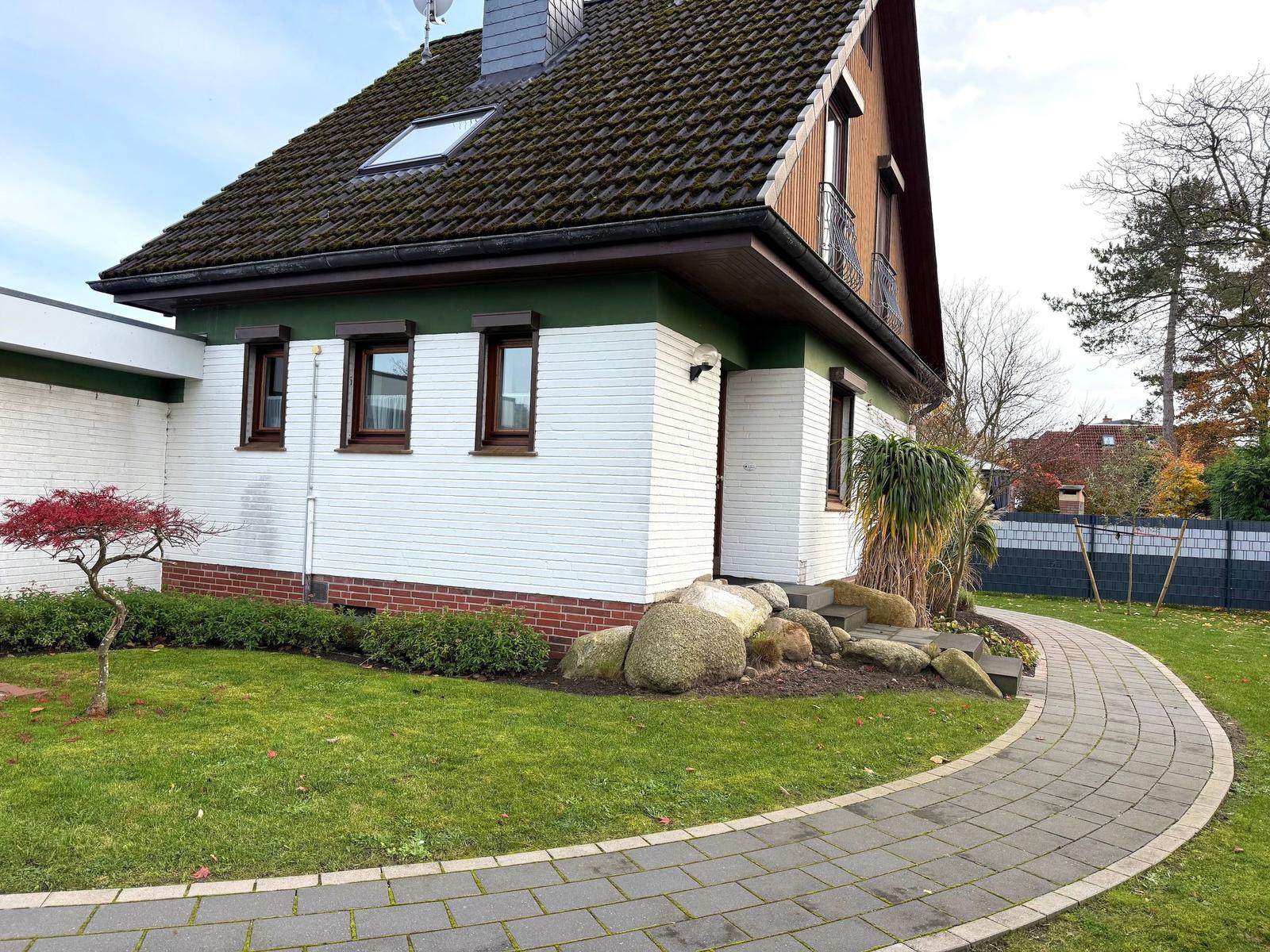 House with white facade, green roof, and landscaped garden with stone path.