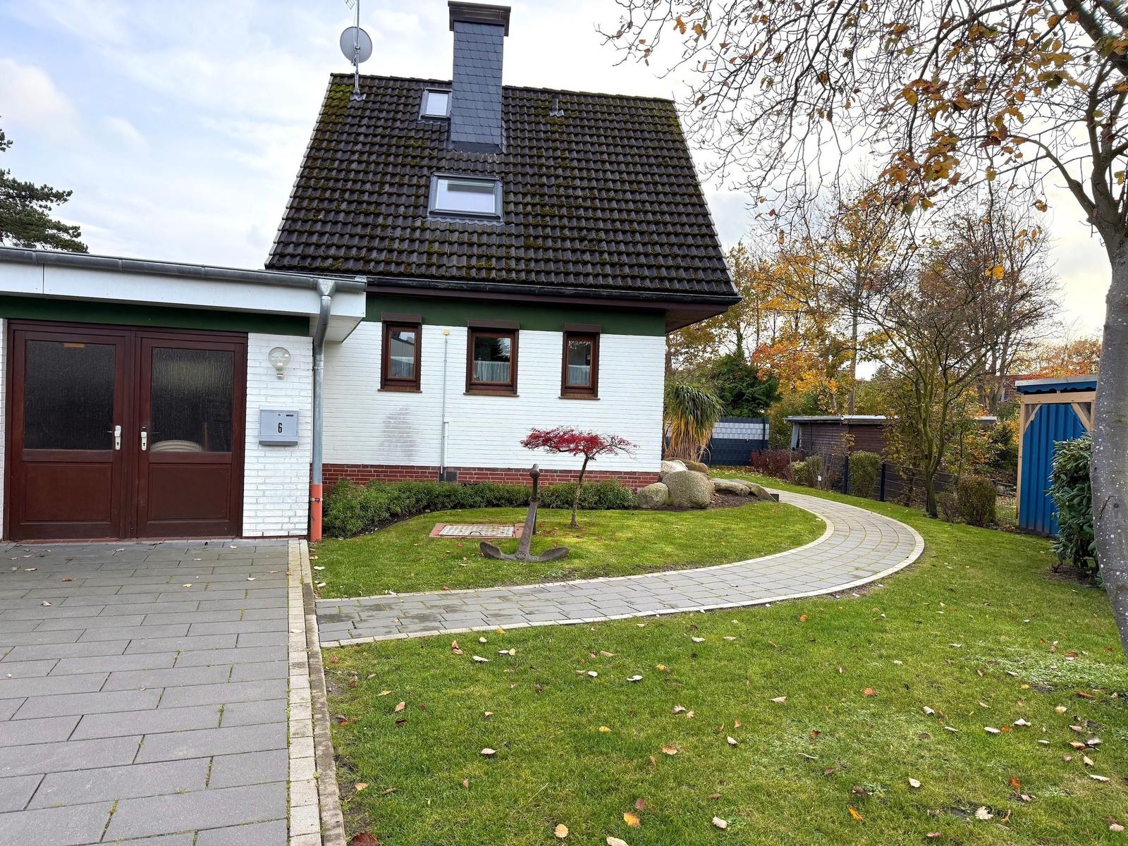 House with garden, stone path, and red tree. Garage and satellite dish.