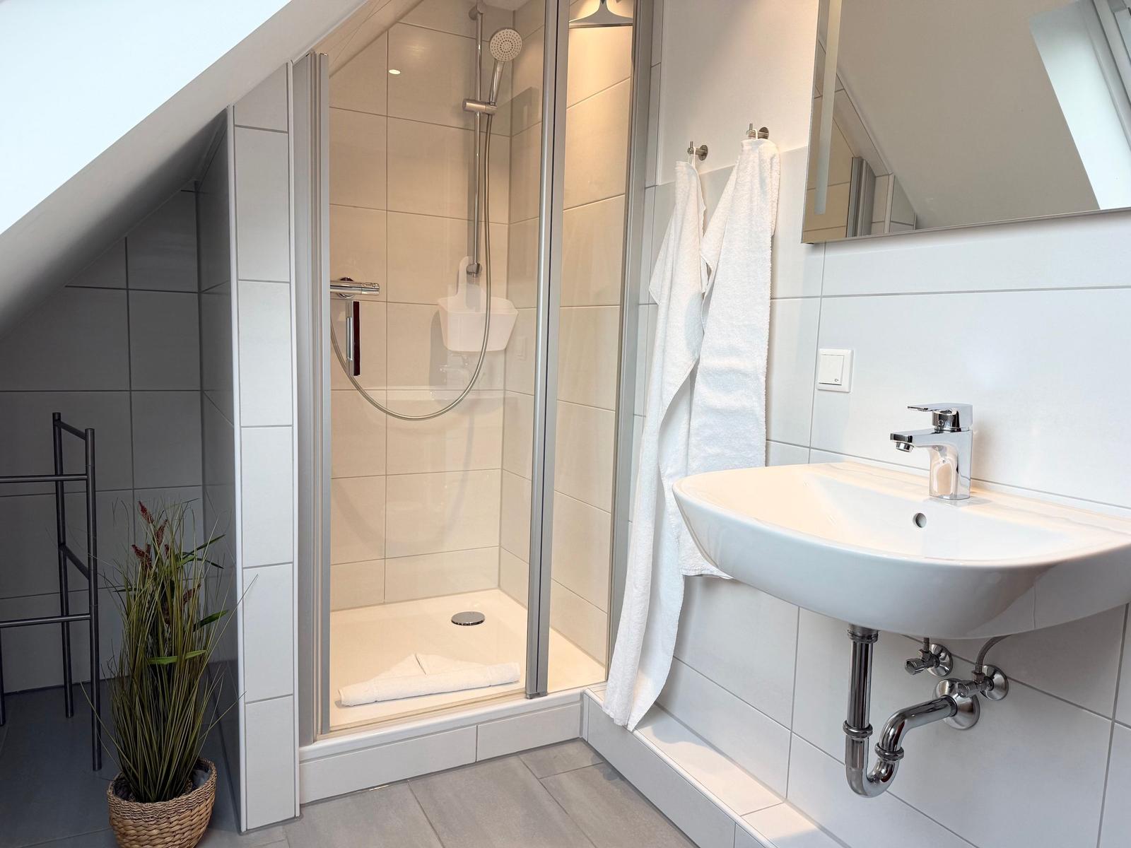 Bathroom with shower, sink, and mirror. White tiles and towel rack.