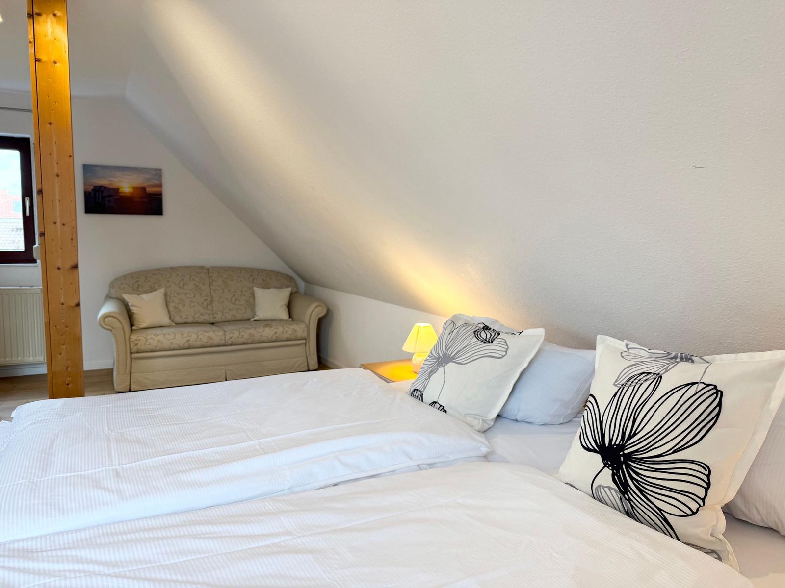 A bedroom with a double bed, sofa, and nightstand under a sloped ceiling.