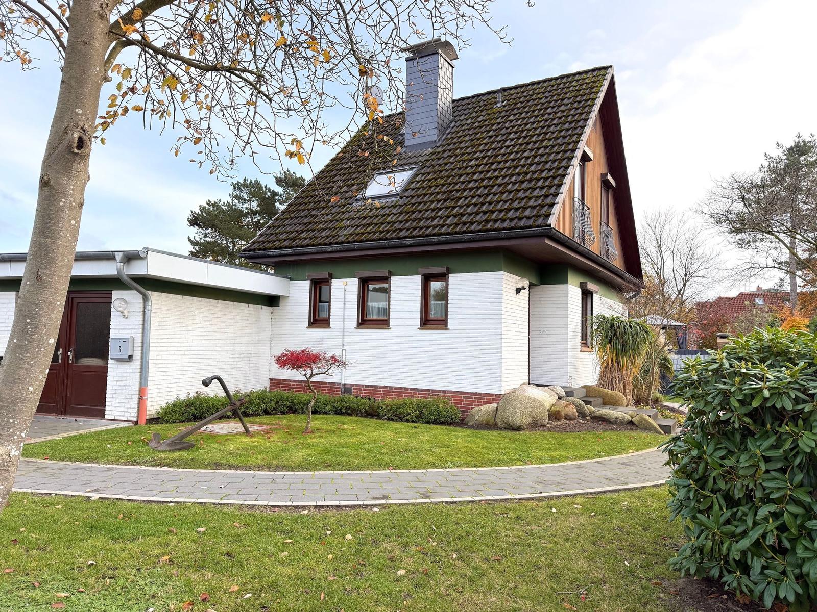 House with white facade, green roof, and garden with stones and trees.