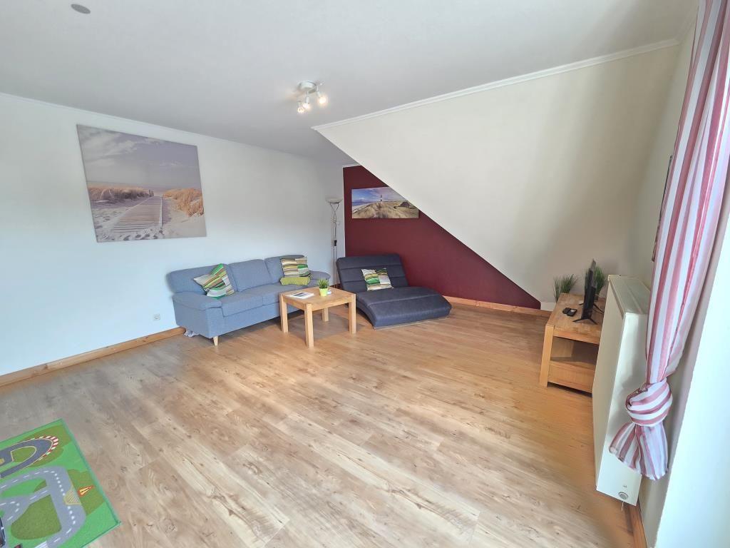 Wohnzimmer mit Sofa, Couch, Tisch und Holzboden. An der Wand hängt ein Bild.