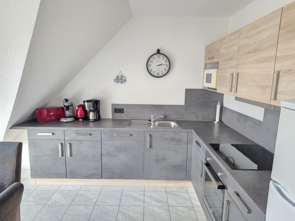 Küche mit grauen Schränken, Arbeitsfläche und Spüle unter schräger Decke.