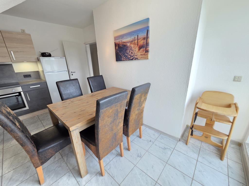 Essbereich mit Holztisch, vier Stühlen und Hochstuhl. Küche mit Kühlschrank und Herd.