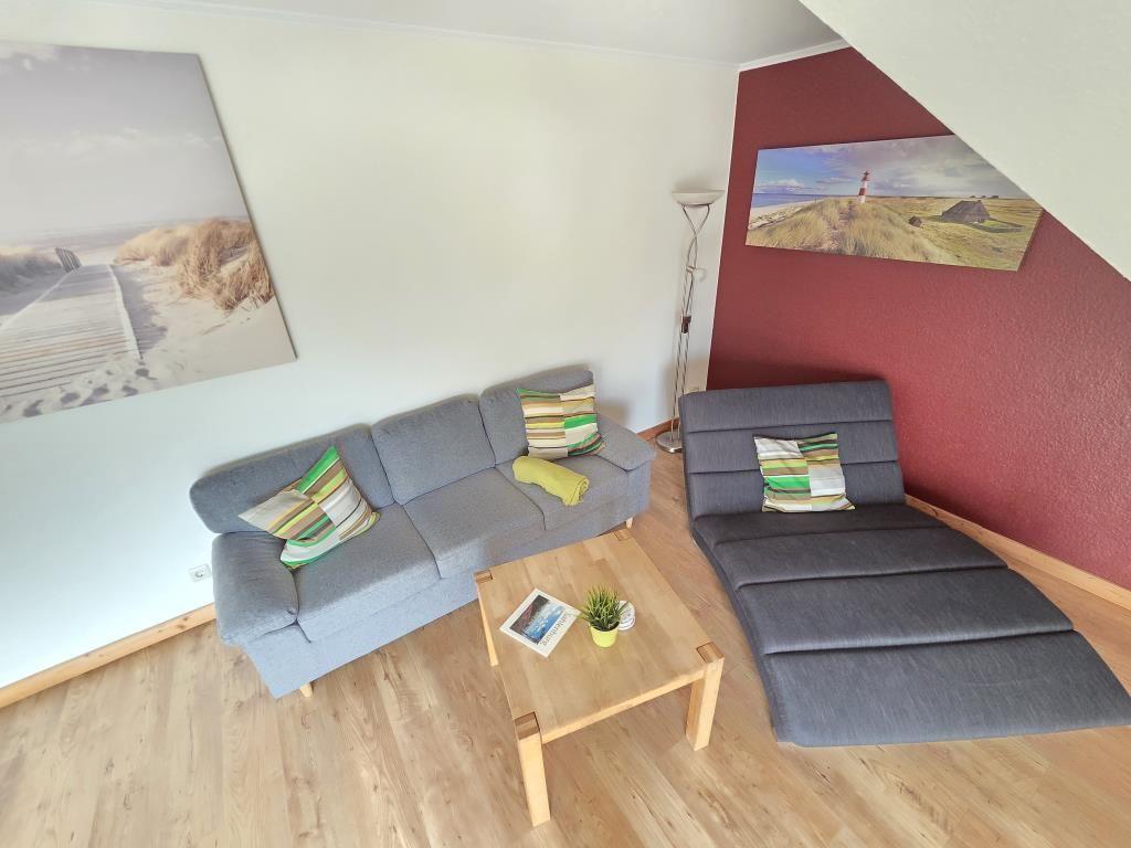 Wohnzimmer mit grauem Sofa, Liege und Holztisch. Wandbilder und Holzboden.