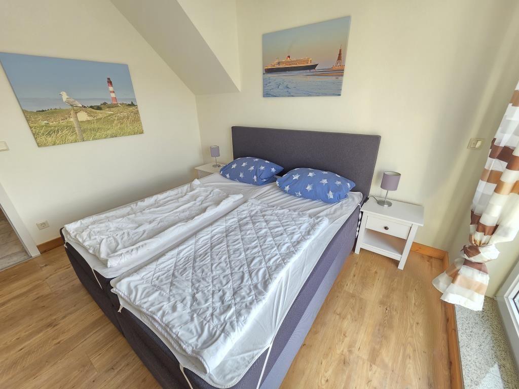Schlafzimmer mit Doppelbett, zwei Nachttischen und Wandbildern an den Wänden.